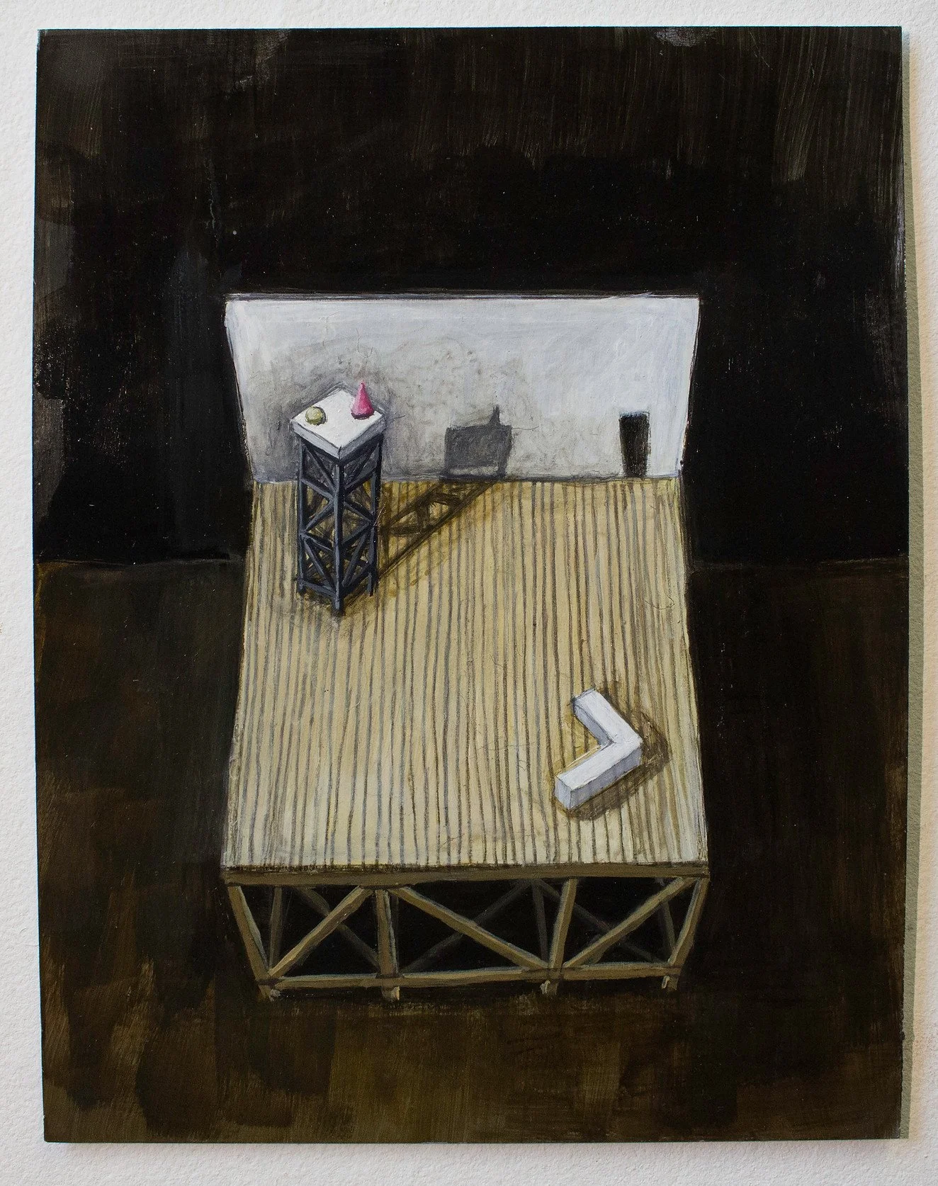 A bird's eye view of a small exhibition space with a wooden platform and dark background, featuring a white 'L'-shaped object and a black stand with small items on top.