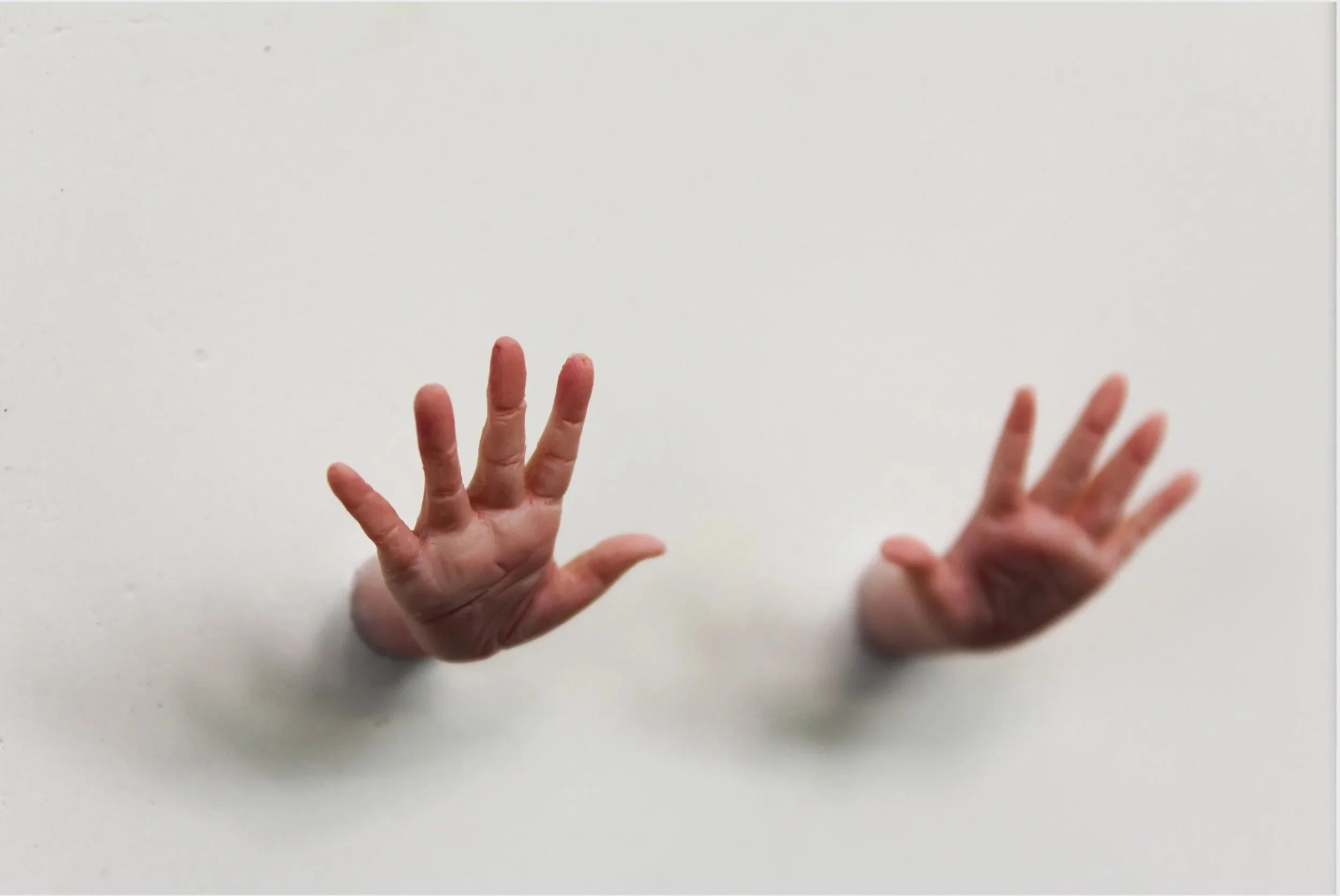 Two disembodied human hands emerging from a white surface, with one hand showing four fingers and the other showing five fingers.