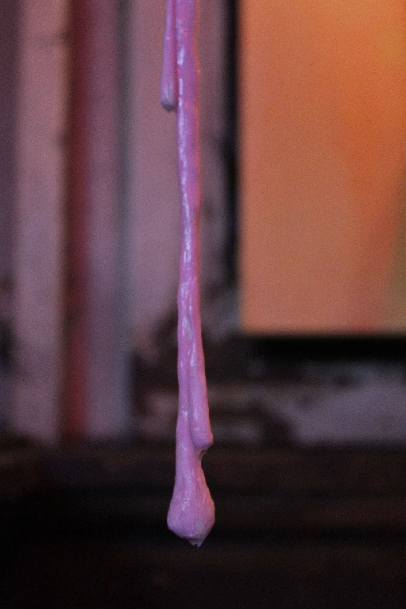 A close-up of pink glue dripping from a surface with a blurred background.