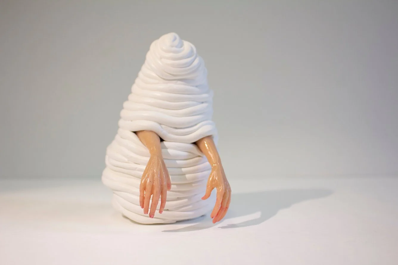 A whimsical sculpture resembling a ghost or blob with elongated arms, made of white twisted material, with human-like hands hanging from the sides.