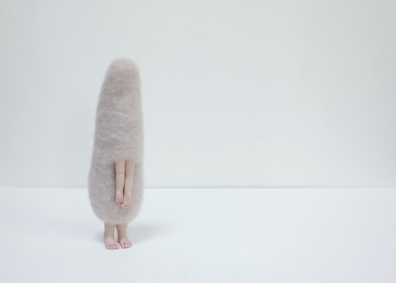 Person standing with their body covered by a fluffy, beige costume that resembles a large, elongated oval shape. Only their bare feet and legs are visible.