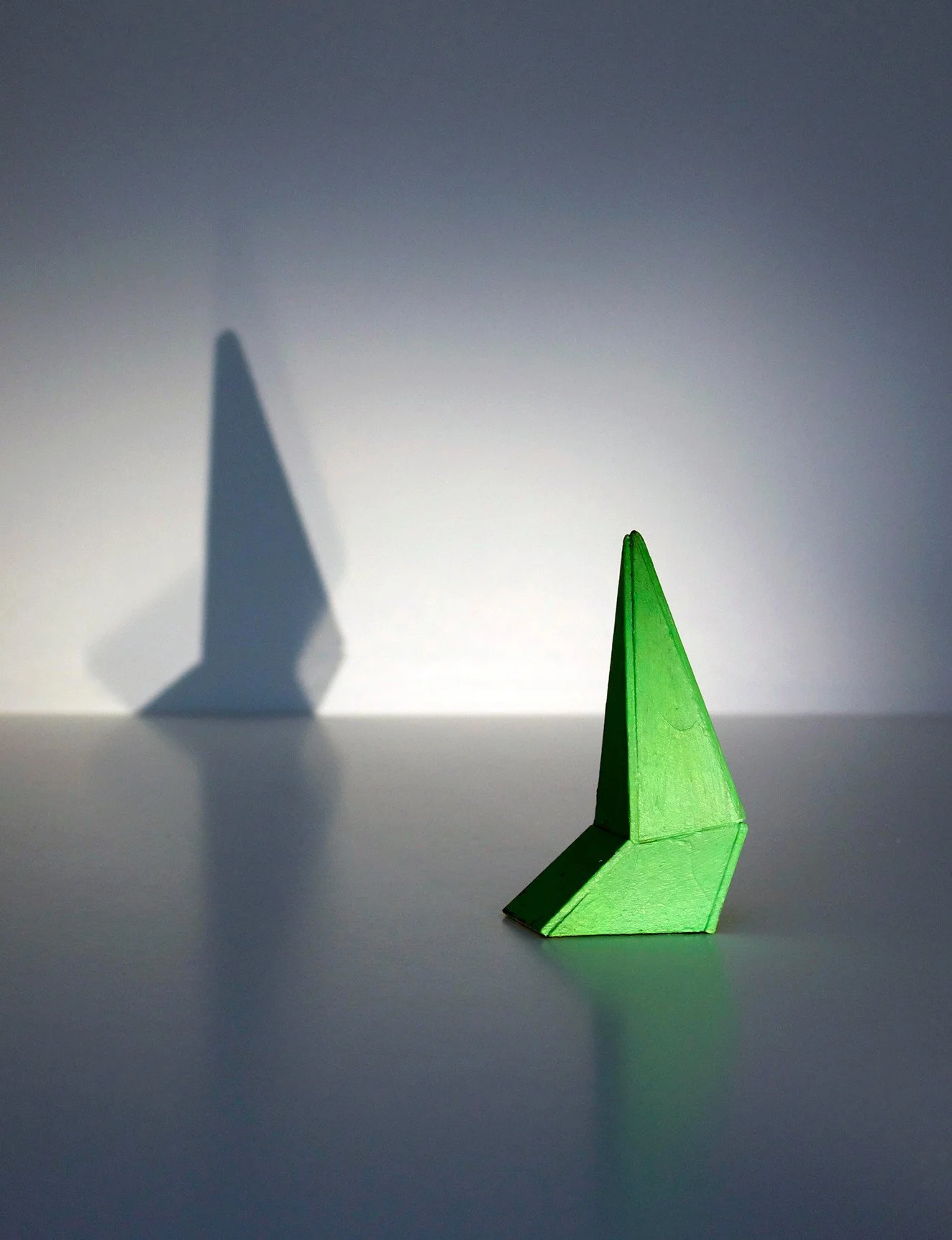 Green origami boat casting a shadow on a plain surface with a gradient background.
