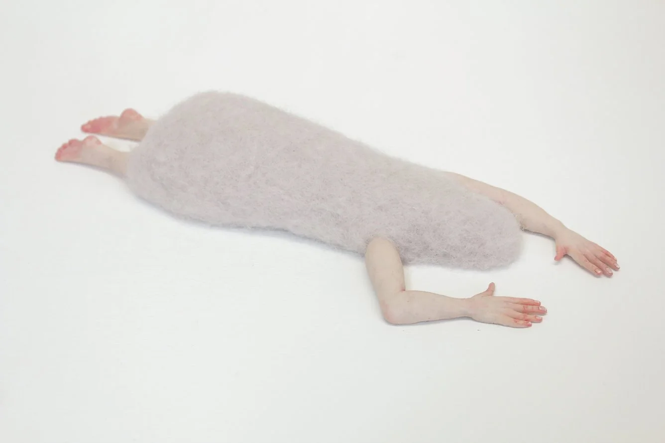 A felted human body lying on a plain white surface.