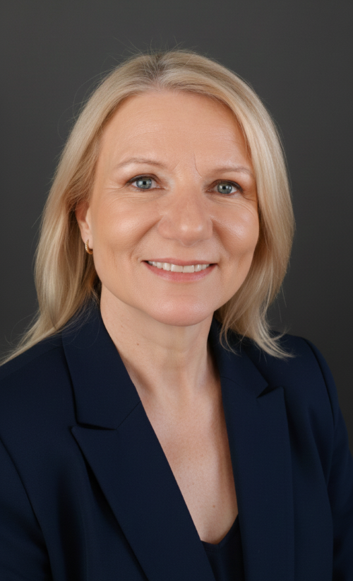A professional woman with blonde hair, blue eyes, wearing a navy blazer, smiling against a dark gray background.