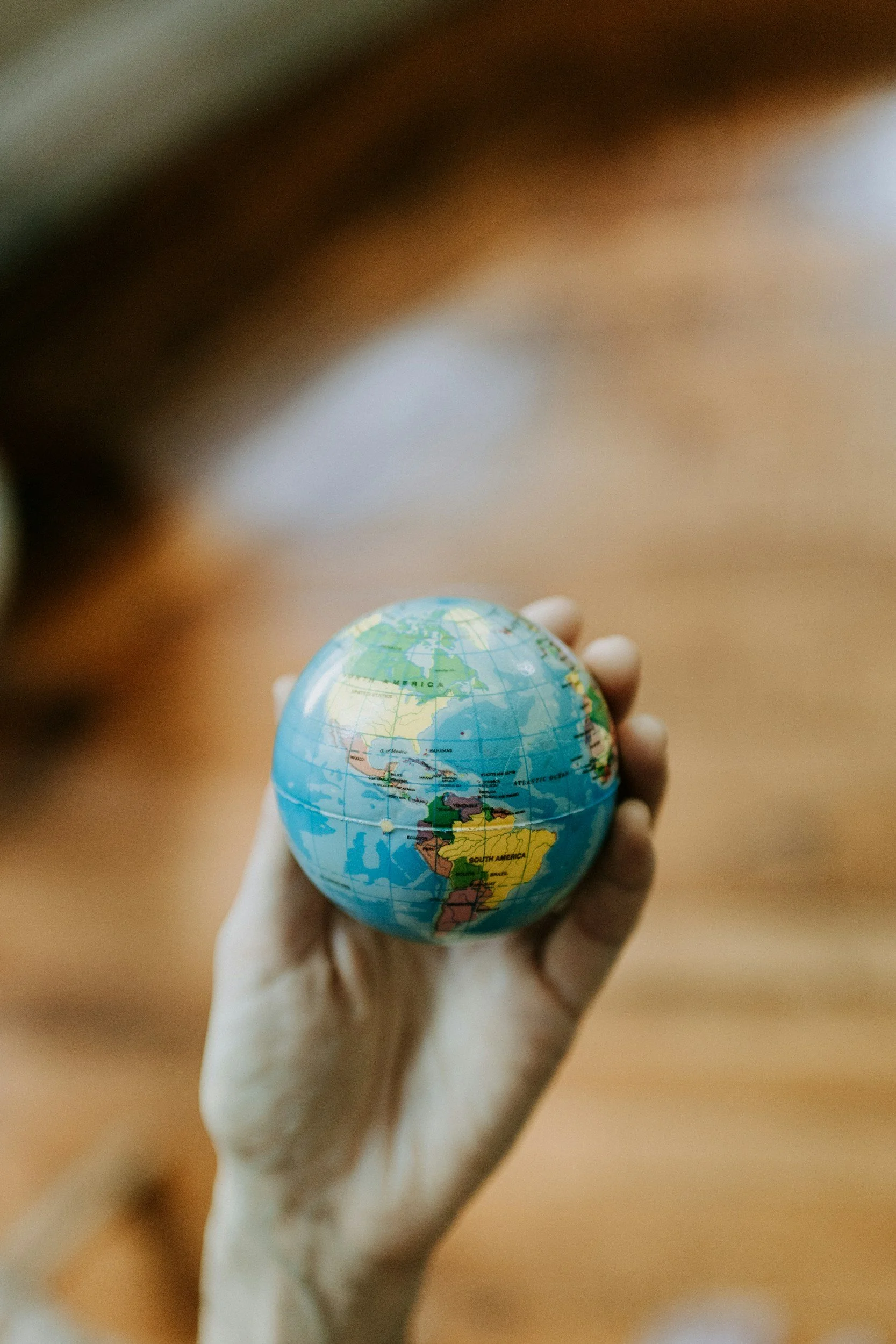 A hand holding a small globe of Earth, showing South America prominently.