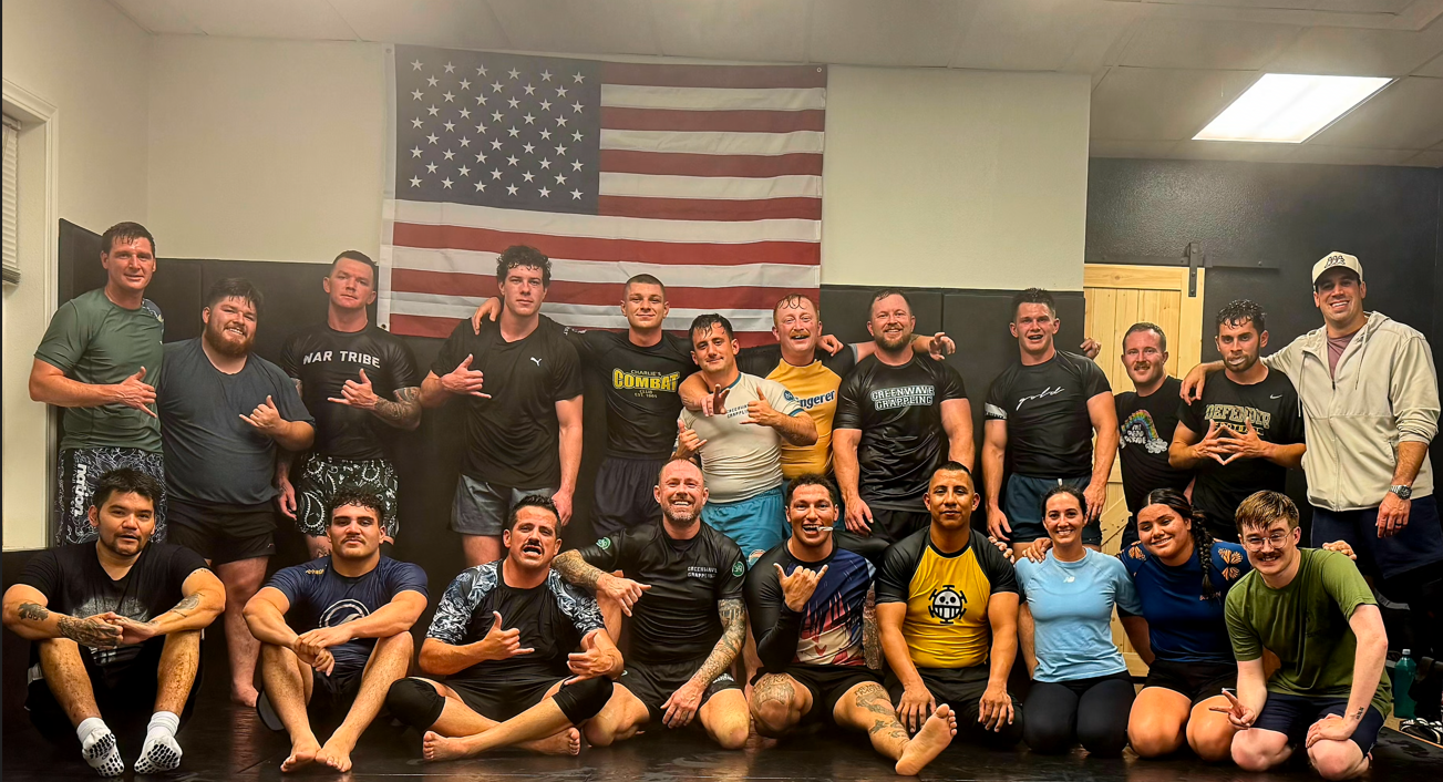 Group of diverse martial artists and fighters posing for a photo in a gym with an American flag in the background.