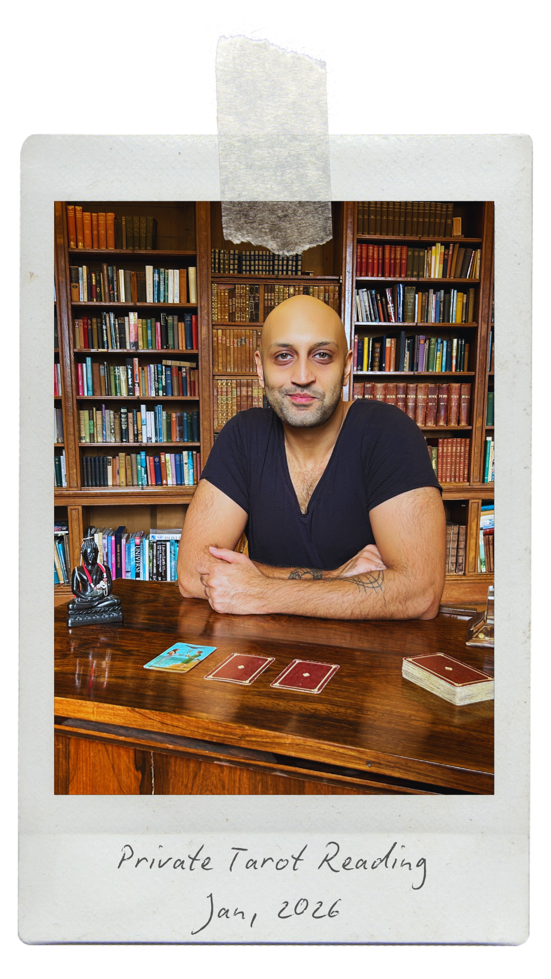 A man with a shaved head and beard sitting at a wooden table with tarot cards. Behind him are bookshelves filled with books. A small statue of a seated figure is on the table. The photo has a white Polaroid-style border with handwritten text at the bottom that says, "Private Tarot Reading Jan, 2026."