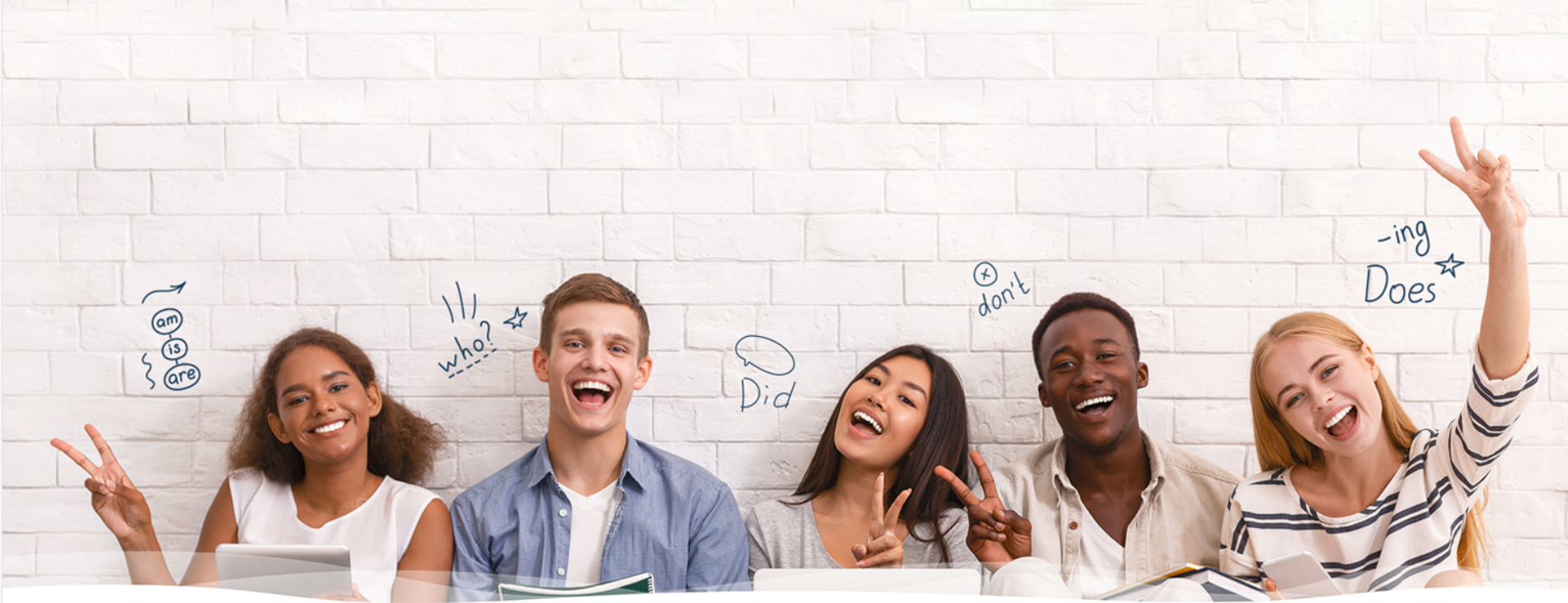 Group of five diverse young adults smiling and making peace signs, sitting in front of a white brick wall with handwritten words and symbols related to grammar questions.