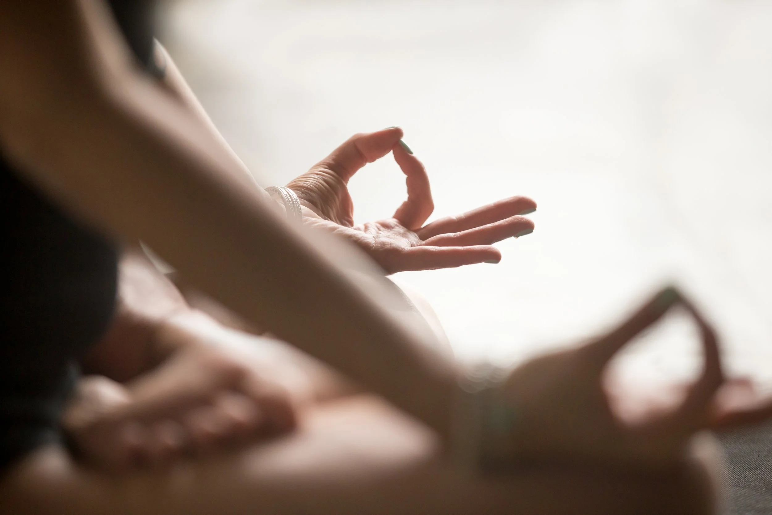 Close-up of a person's hand practicing yoga or meditation, making an 'okay' gesture with their thumb and index finger, with a blurred background.