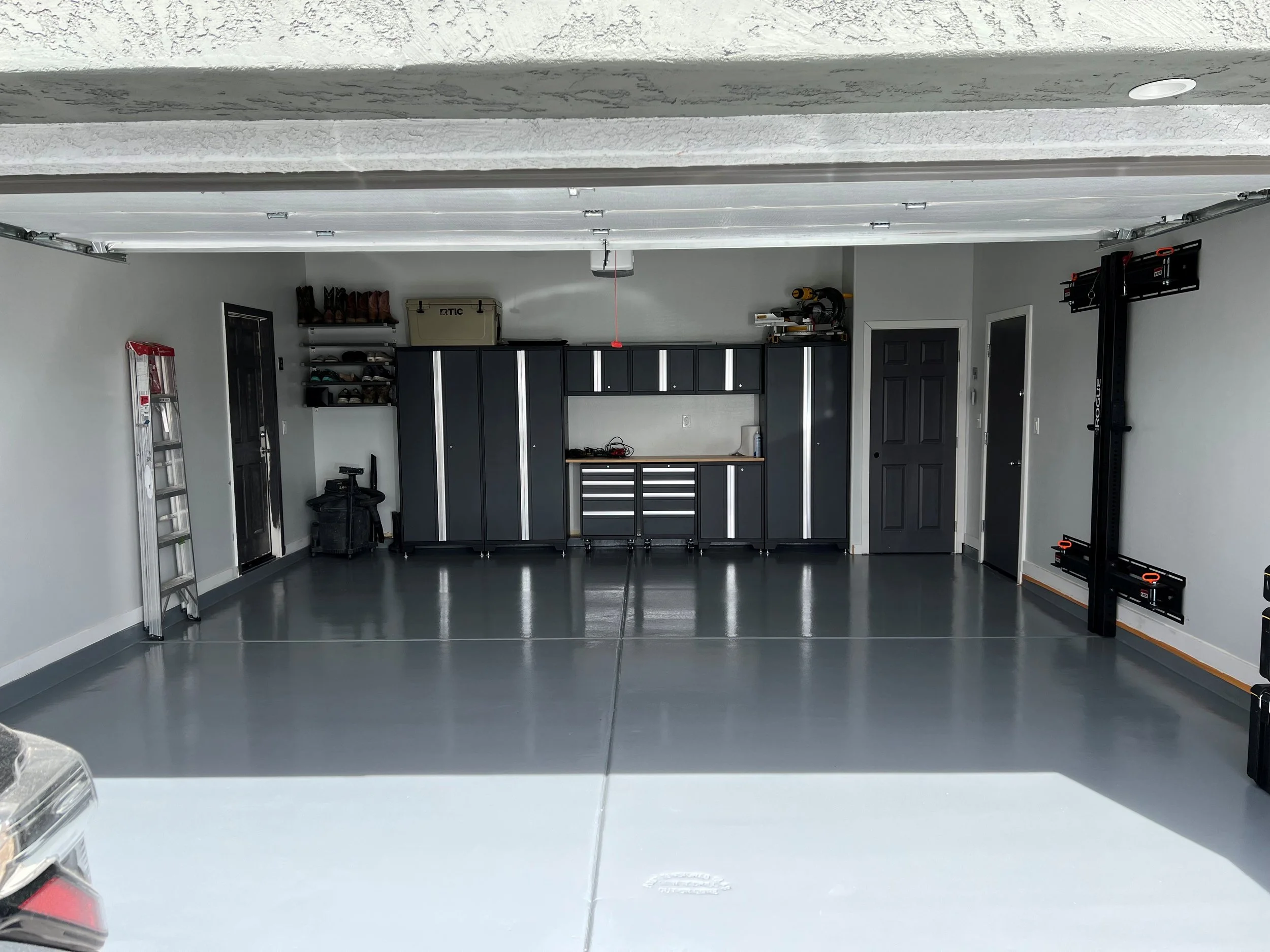 Empty garage with organized tools, cabinets, and a ladder.