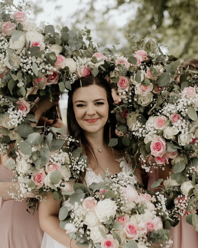 A bride surrounded by bridesmaids' bouquets held in the shape of a heart around her face.
