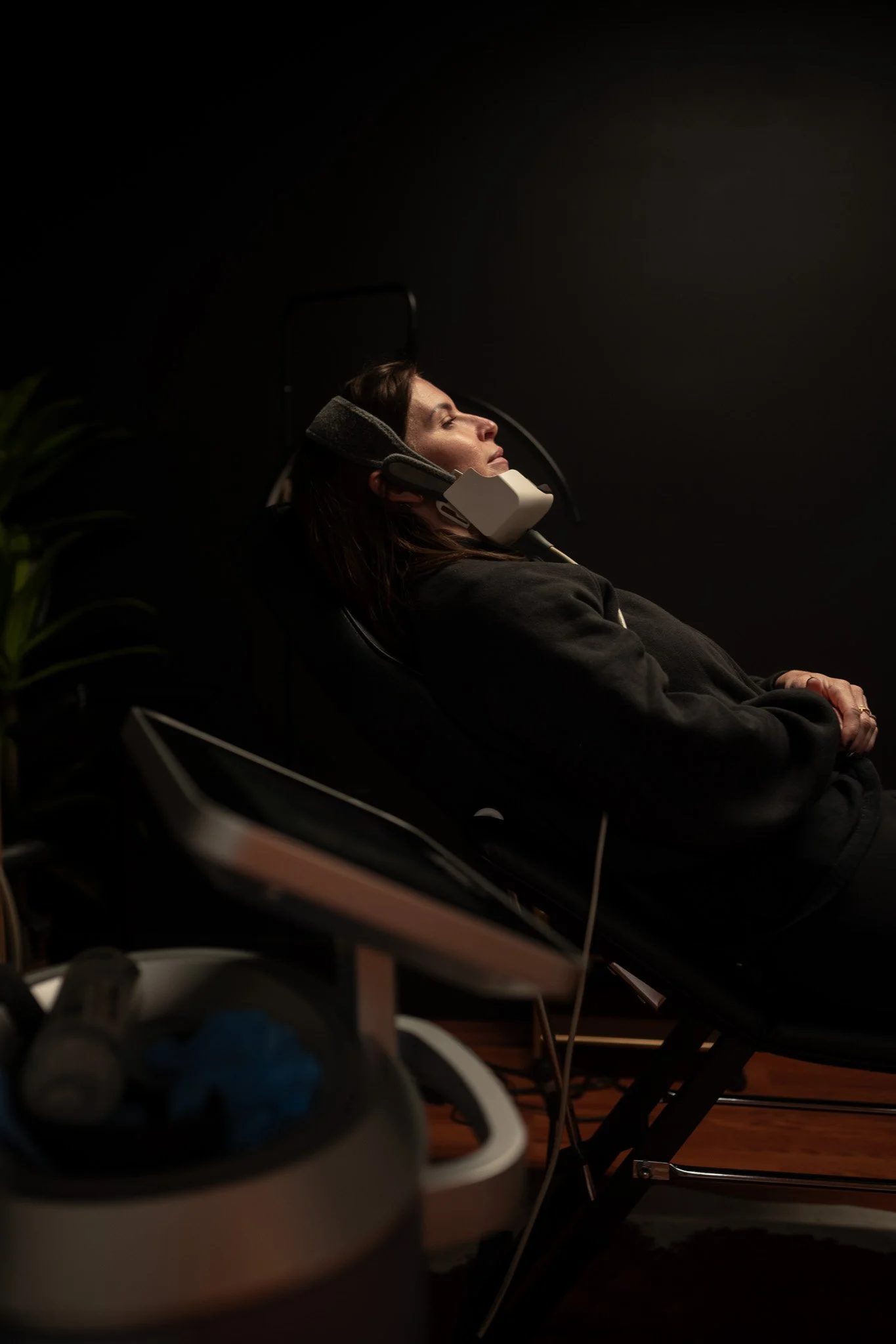 A woman relaxing in a reclined chair with an eye mask and headphones, appearing to rest or meditate in a dimly lit room.