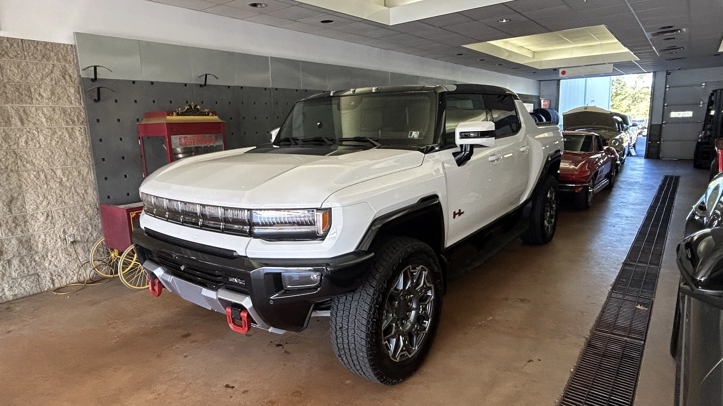 A large white and black electric pickup truck parked inside a garage with other vintage and modern cars.