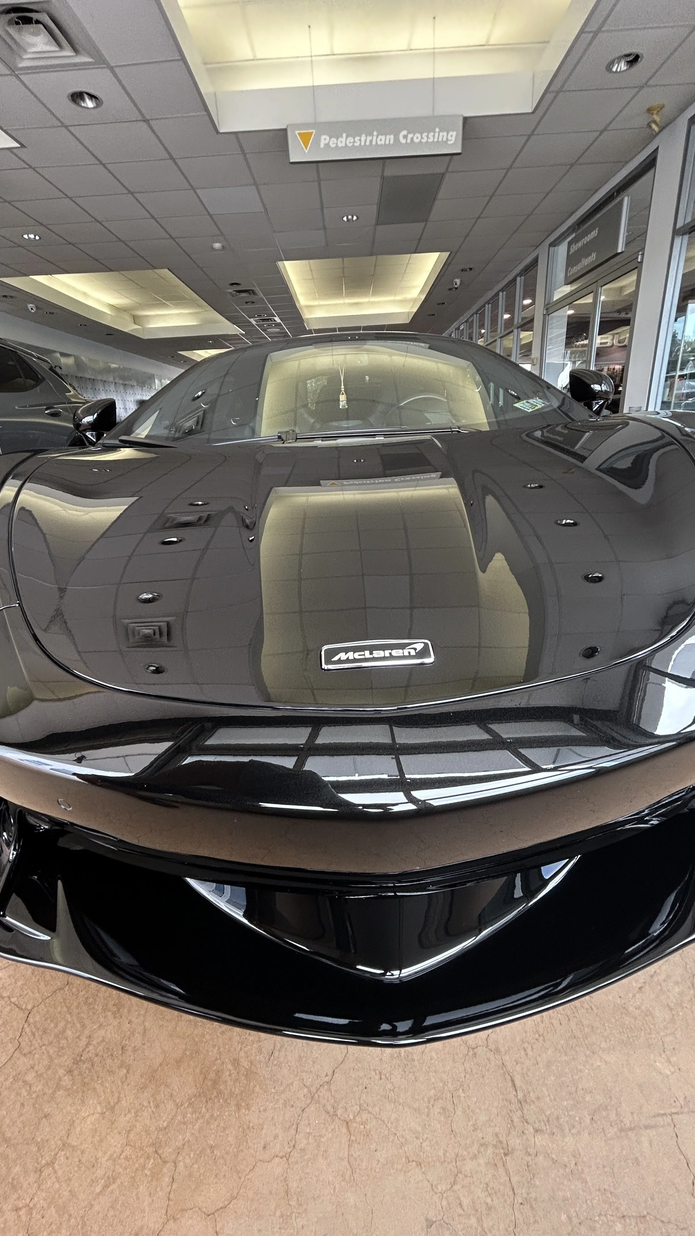 Front view of a black McLaren sports car inside a dealership showroom, reflecting the ceiling lights.