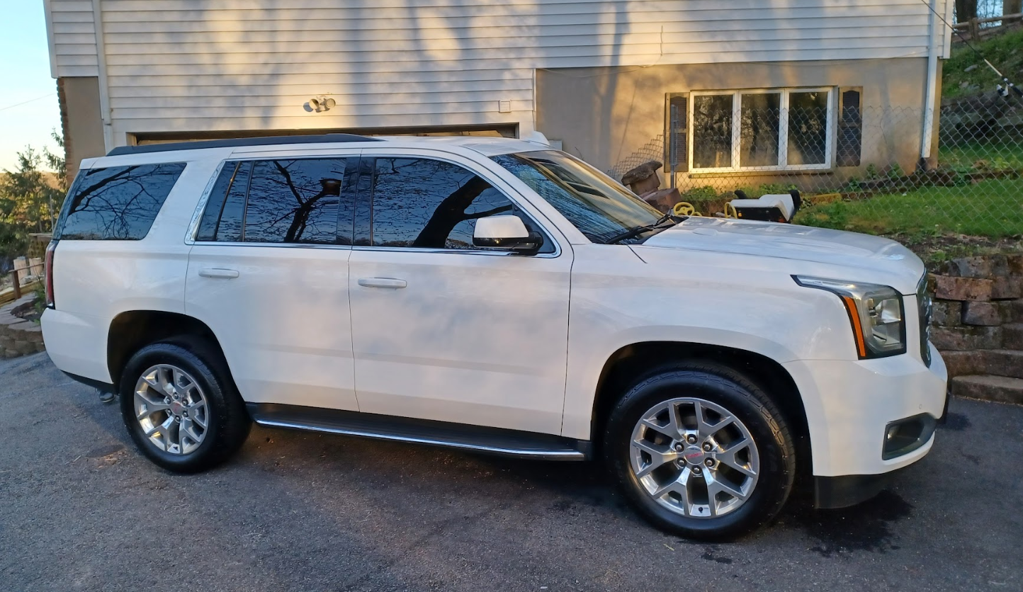 Silver SUV parked on driveway near house with a fence and yard.