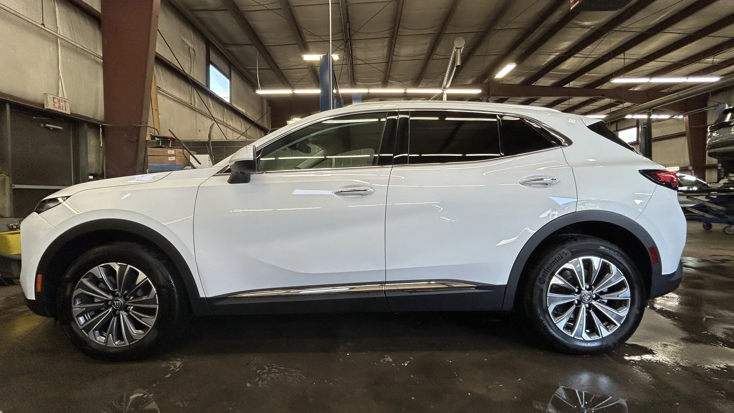 White Audi SUV inside a garage with a high ceiling and fluorescent lighting, parked near a wall with various tools and equipment visible.