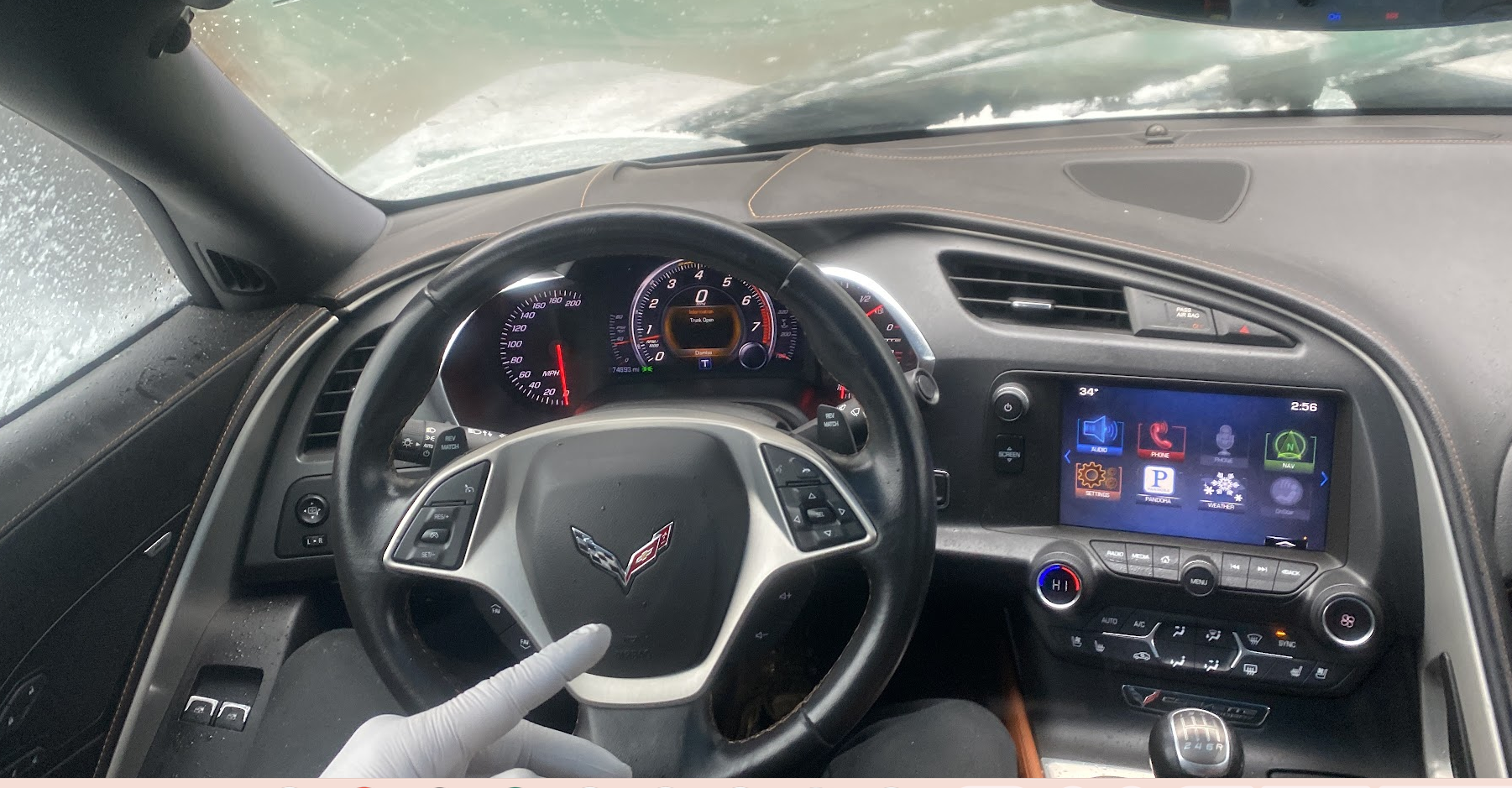 Inside view of a Chevrolet Corvette steering wheel, dashboard, and infotainment system with snowy windshield visible through the front window.