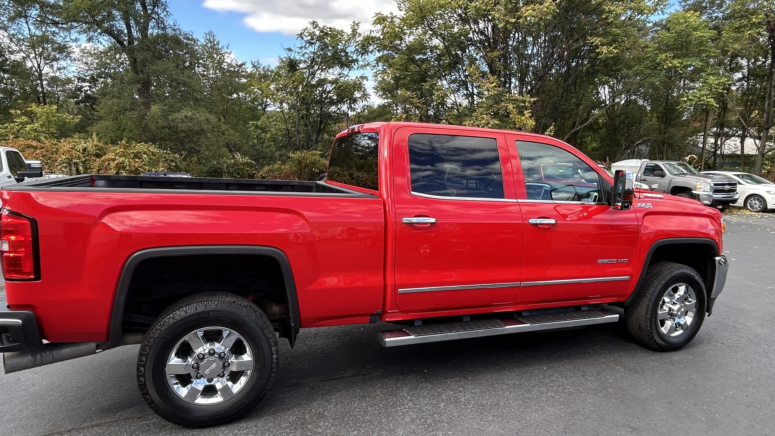 Red pickup truck parked in a lot with trees in the background.