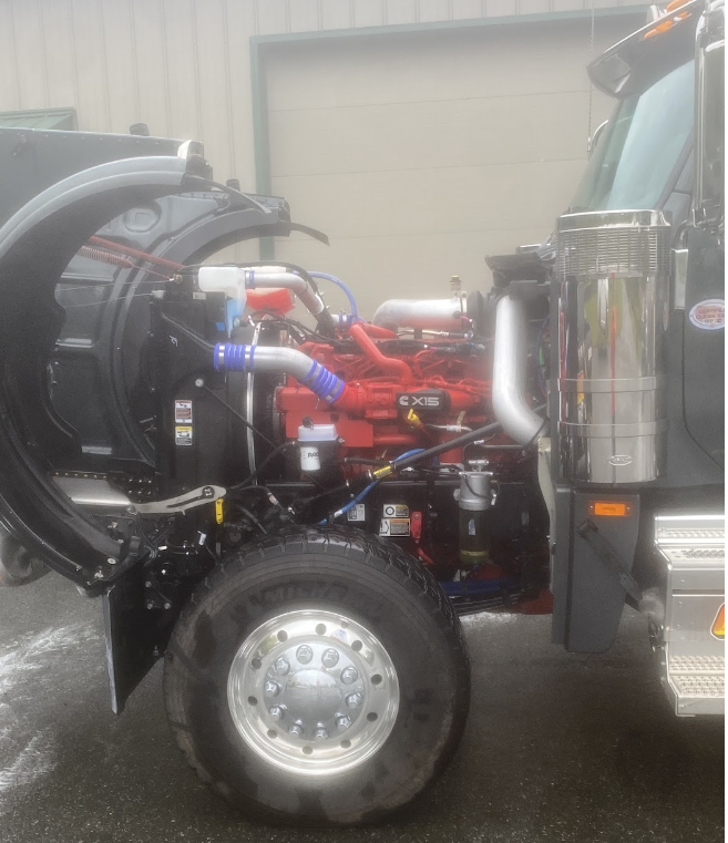 Close-up of a large semi-truck with the hood open, revealing the red engine and various mechanical components.