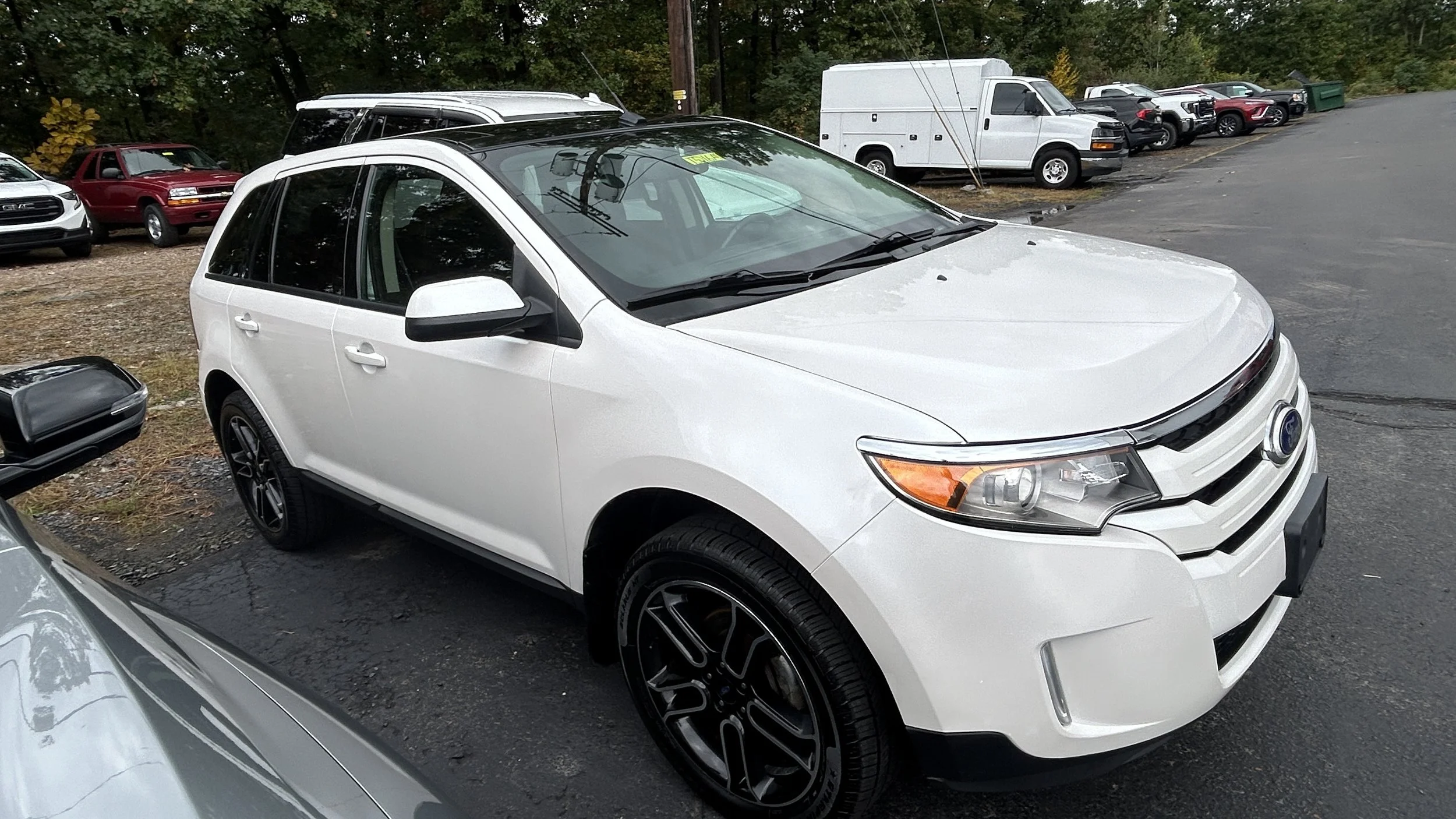 White SUV parked in a lot with other vehicles and trees in the background.