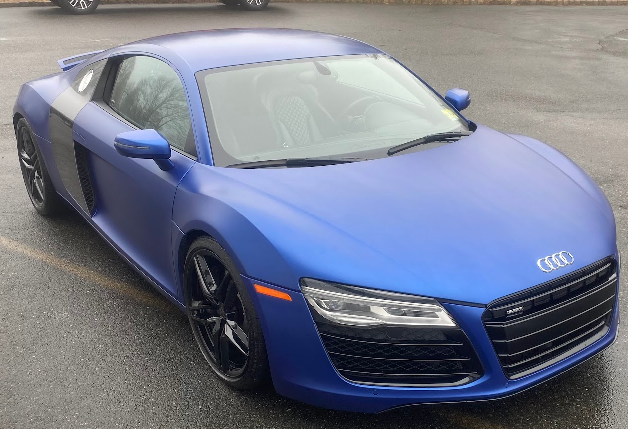 Blue Audi sports car parked on a paved surface, with a black grille and sleek design.