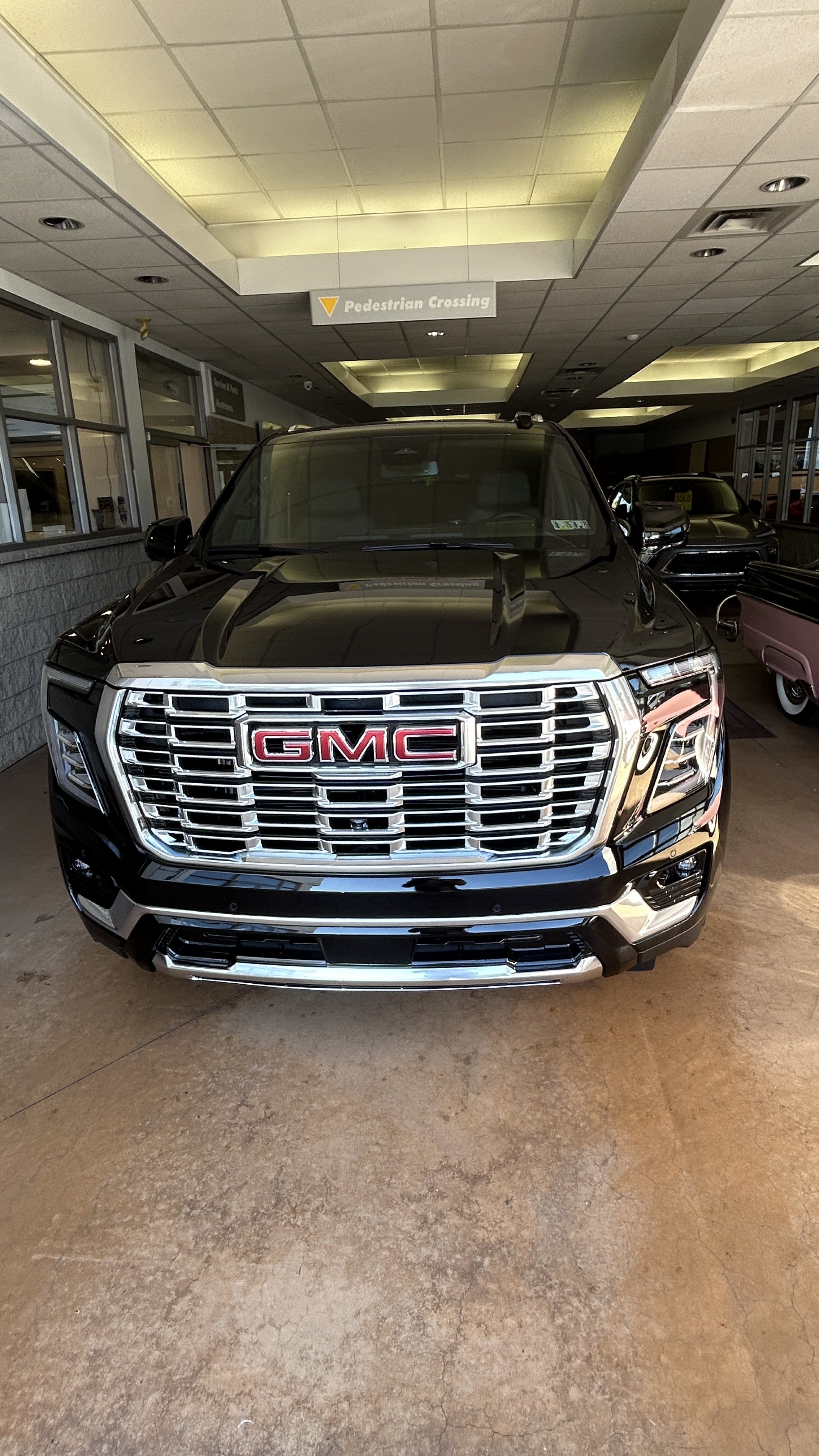 A black GMC SUV parked indoors at a dealership, with a large chrome grille and notable GMC logo on the front.
