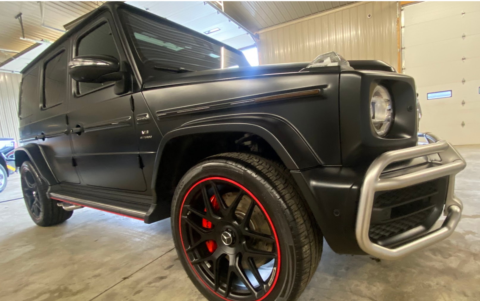 A black luxury SUV with custom red-accented black wheels and chrome bumper guard parked inside a garage.