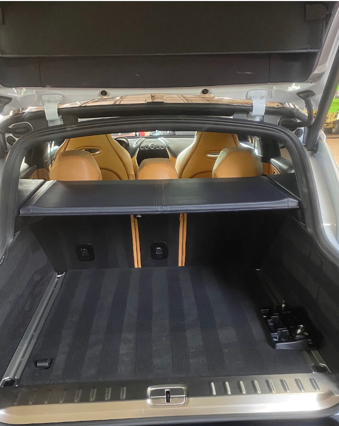 View of the open trunk of a luxury SUV with tan leather seats visible through the rear window, and the cargo area covered by a black parcel shelf.
