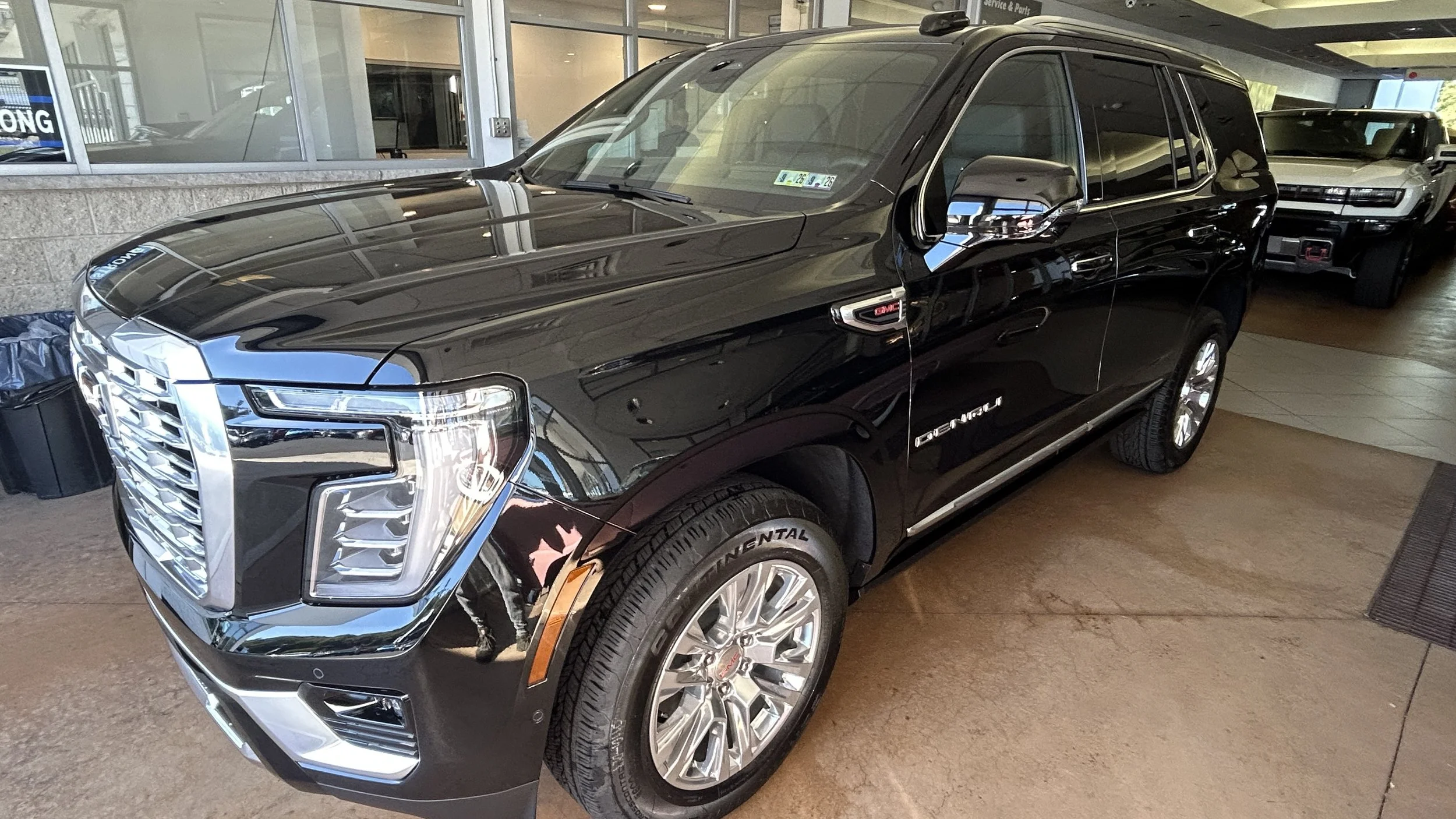 A black GMC Yukon Denali SUV parked inside a dealership showroom with other vehicles visible in the background.