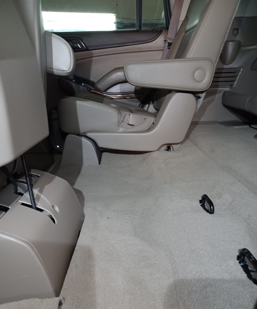 Interior of a beige minivan with a single folded-down middle-row seat and black features; the carpeted floor is visible with two black floor anchors.