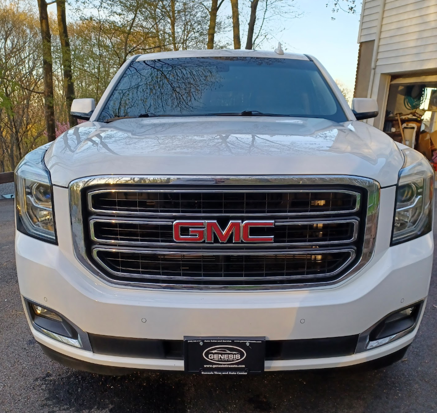 White GMC SUV parked in front of a house with trees in the background.