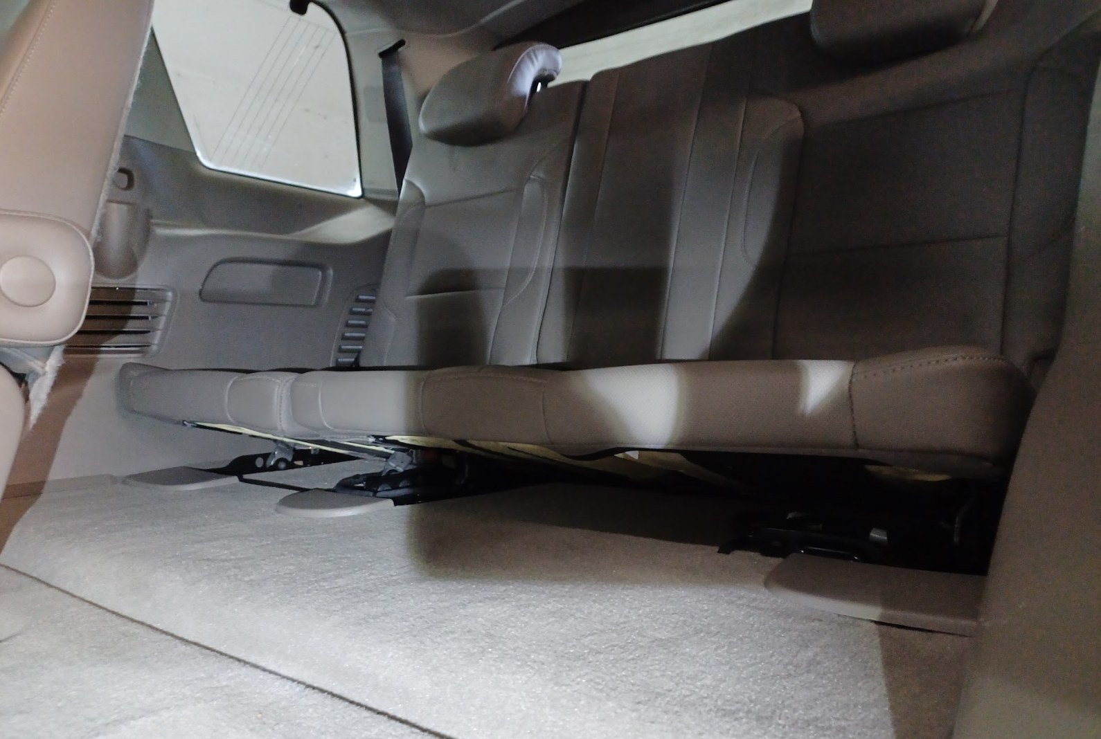 Interior view of a vehicle's third-row back seats, showing gray leather seats, headrests, and part of the beige interior ceiling.