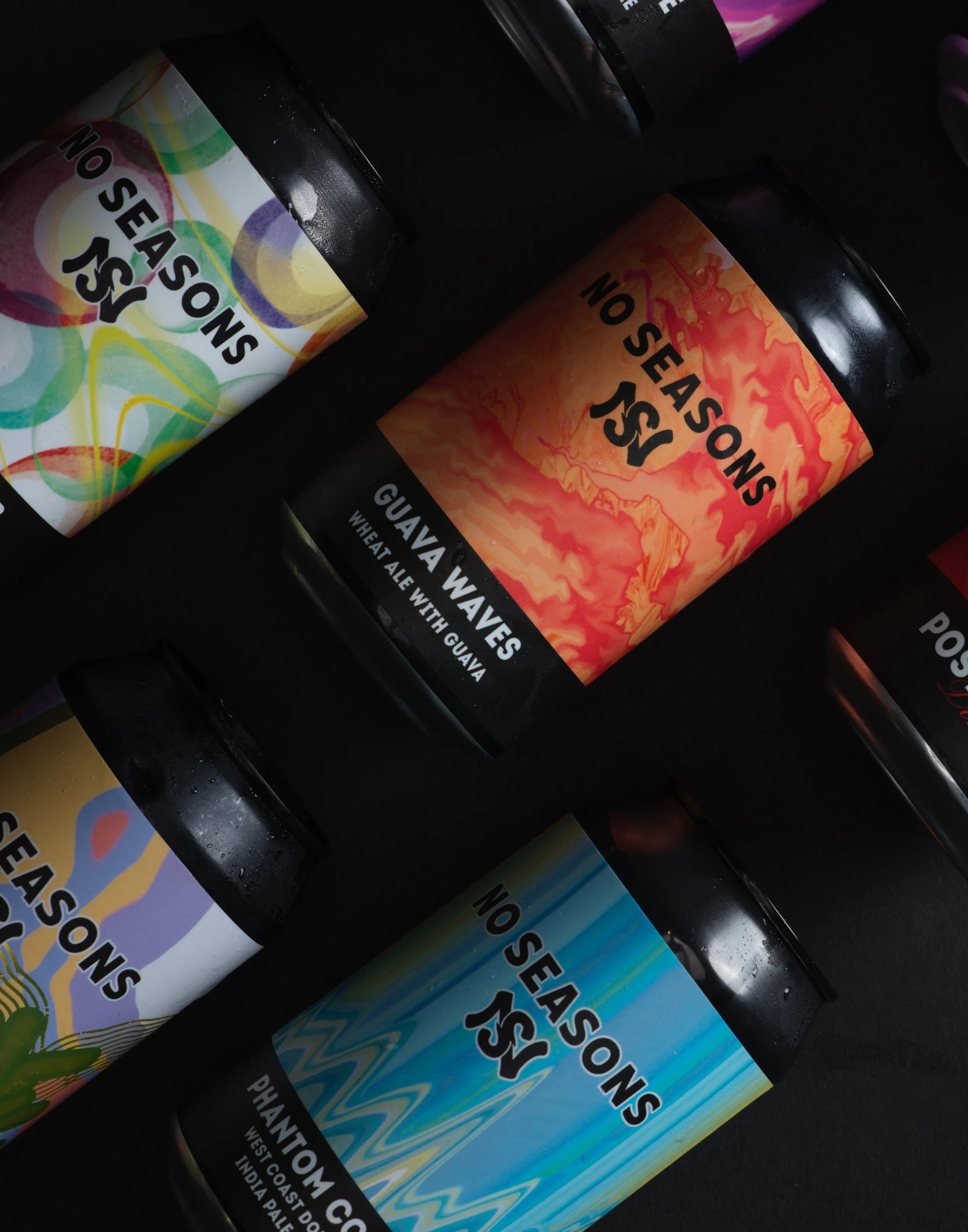 Four cans of No Seasons sparkling beverages with colorful, abstract label designs, including flavors such as Guava Waves, Phantom Coast, and others, arranged on a dark surface.