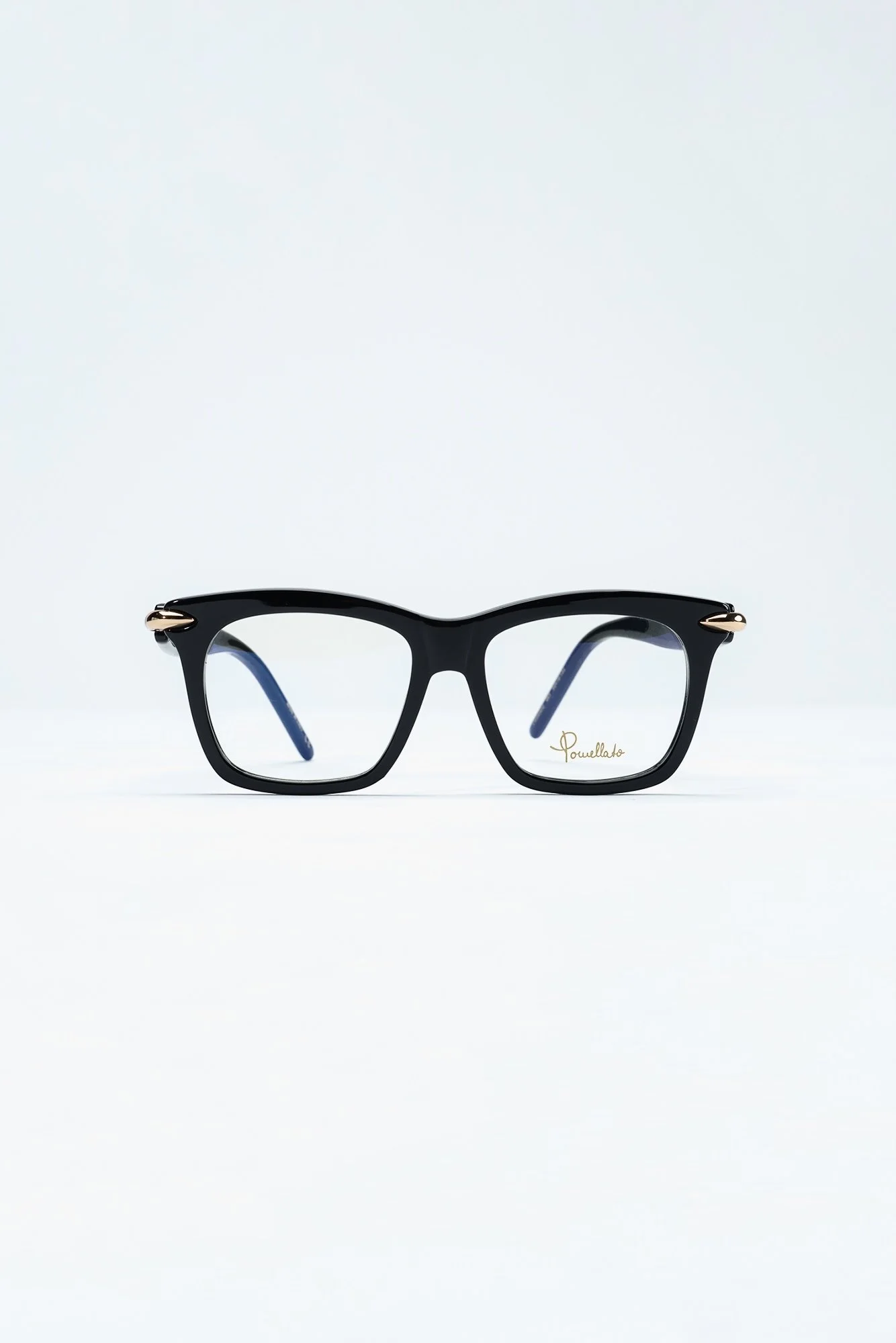 Black eyeglasses with gold accents on the temples, resting on a white surface against a plain white background.