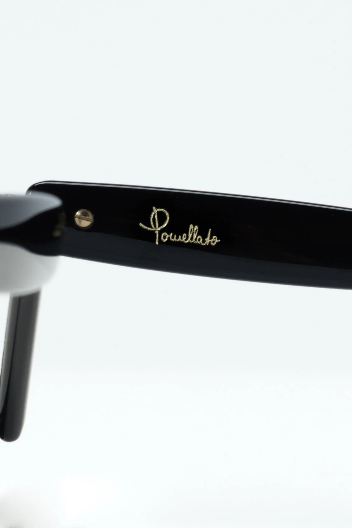 Close-up of the inside arm of black designer sunglasses with gold signature 'Pouillato' on the inner side.
