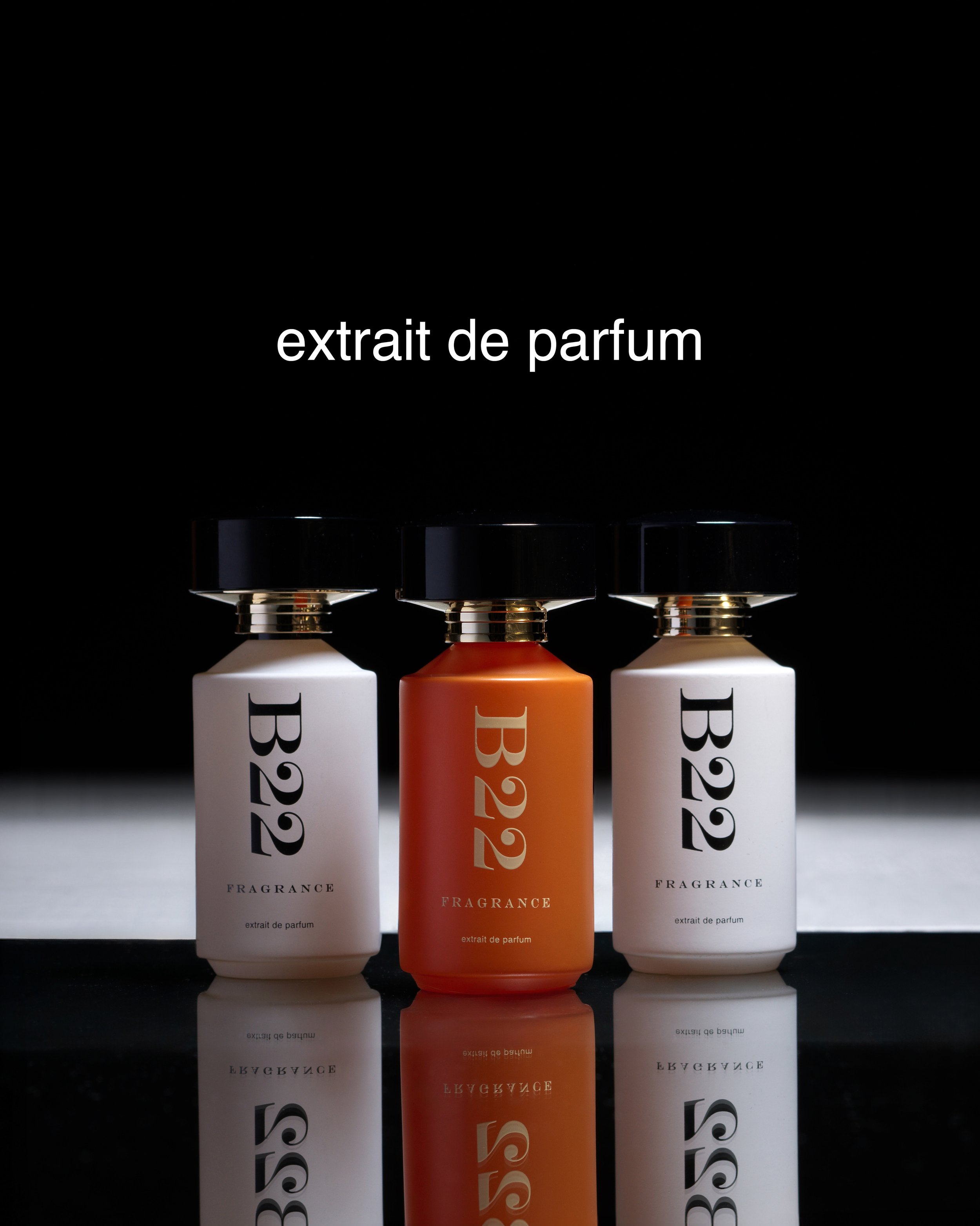 Three bottles of fragrance extract with black caps, two white and one orange, placed on a reflective surface against a dark background, with the text 'extrait de parfum' above.