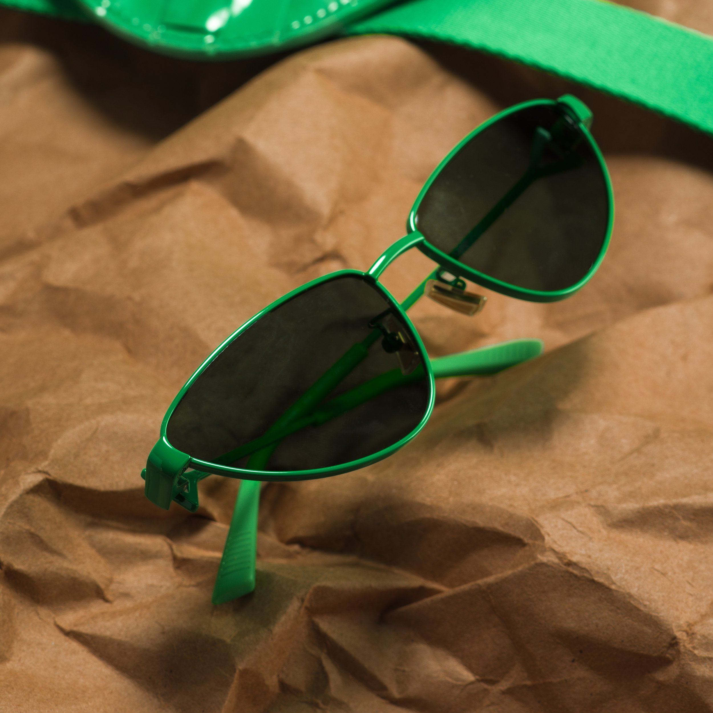 Green sunglasses with dark lenses resting on crumpled brown paper.