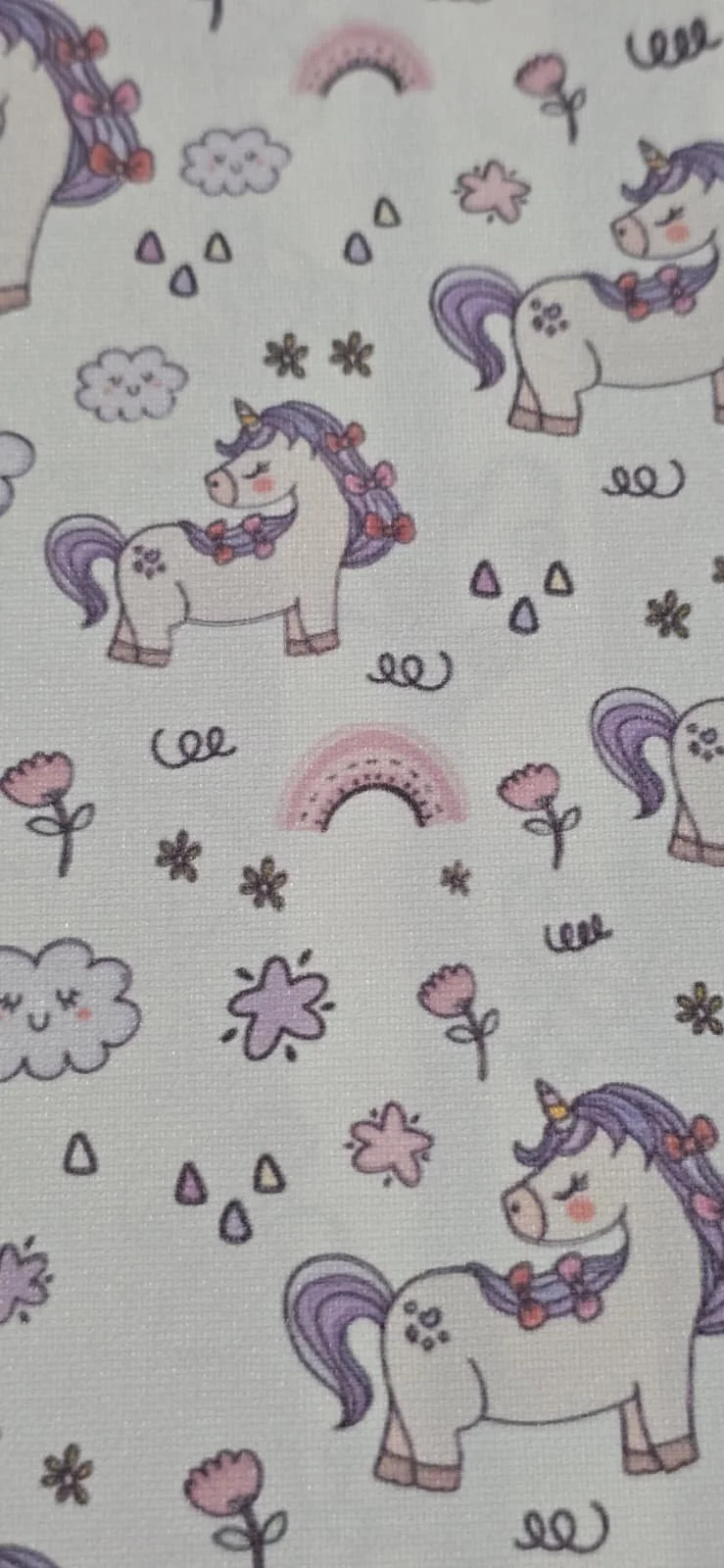 Pattern featuring cartoon pastel-colored unicorns with purple manes and tails, pink flowers, rainbows, clouds, and small decorative elements on a white background.