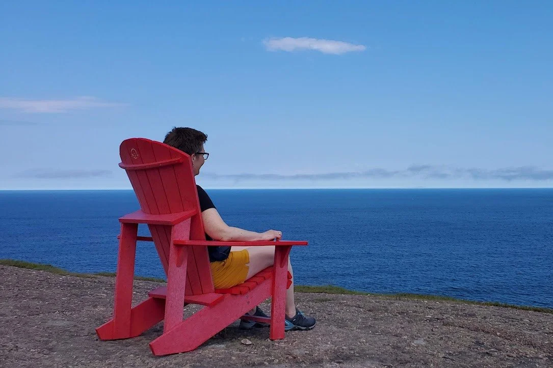 Person sitting on a red Adirondack chair overlooking the ocean on a clear day.