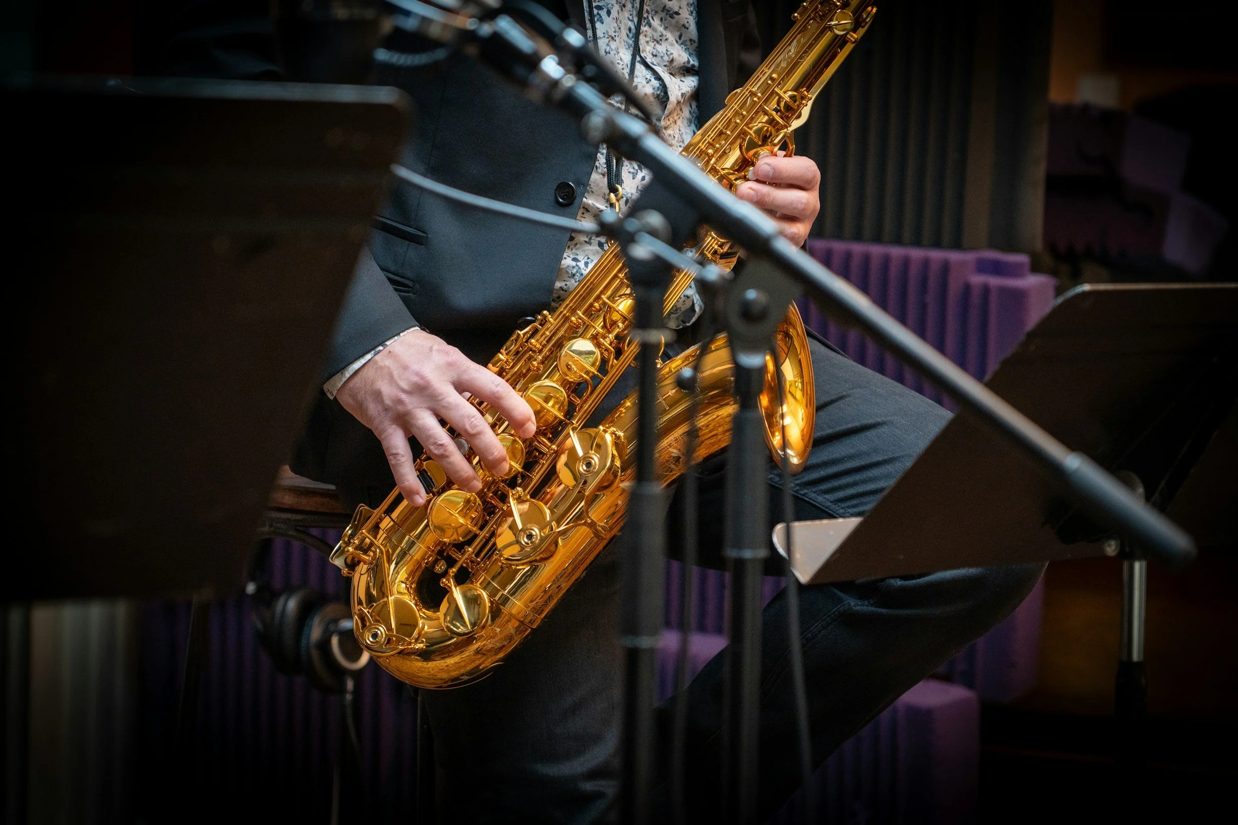 A person playing a gold-colored saxophone in a music studio or concert hall.