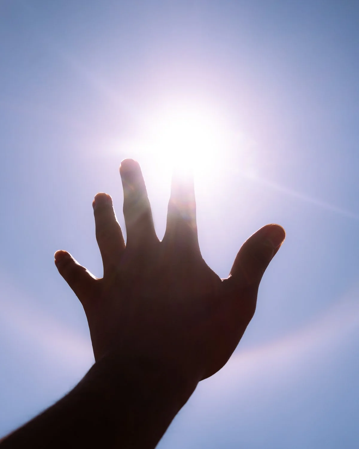 Conceptual photograph by Amador Z of a hand touching the sun with a rainbow