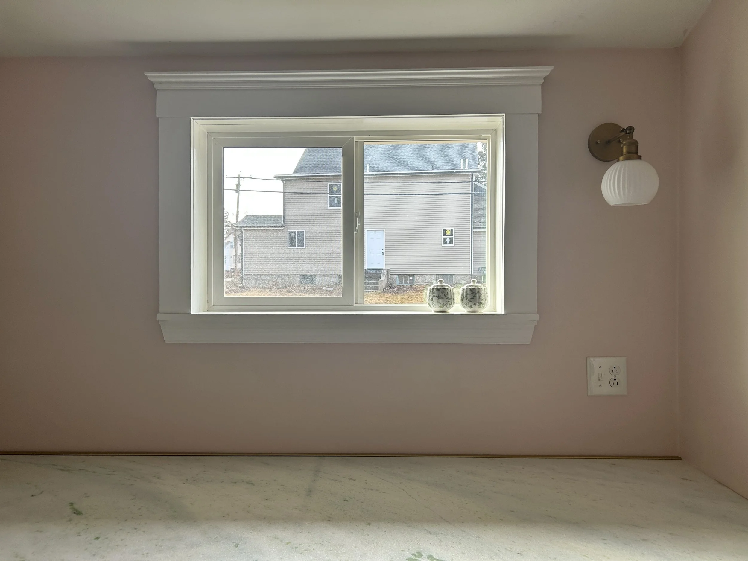Empty room with a window, a wall-mounted light fixture, and an electrical outlet.