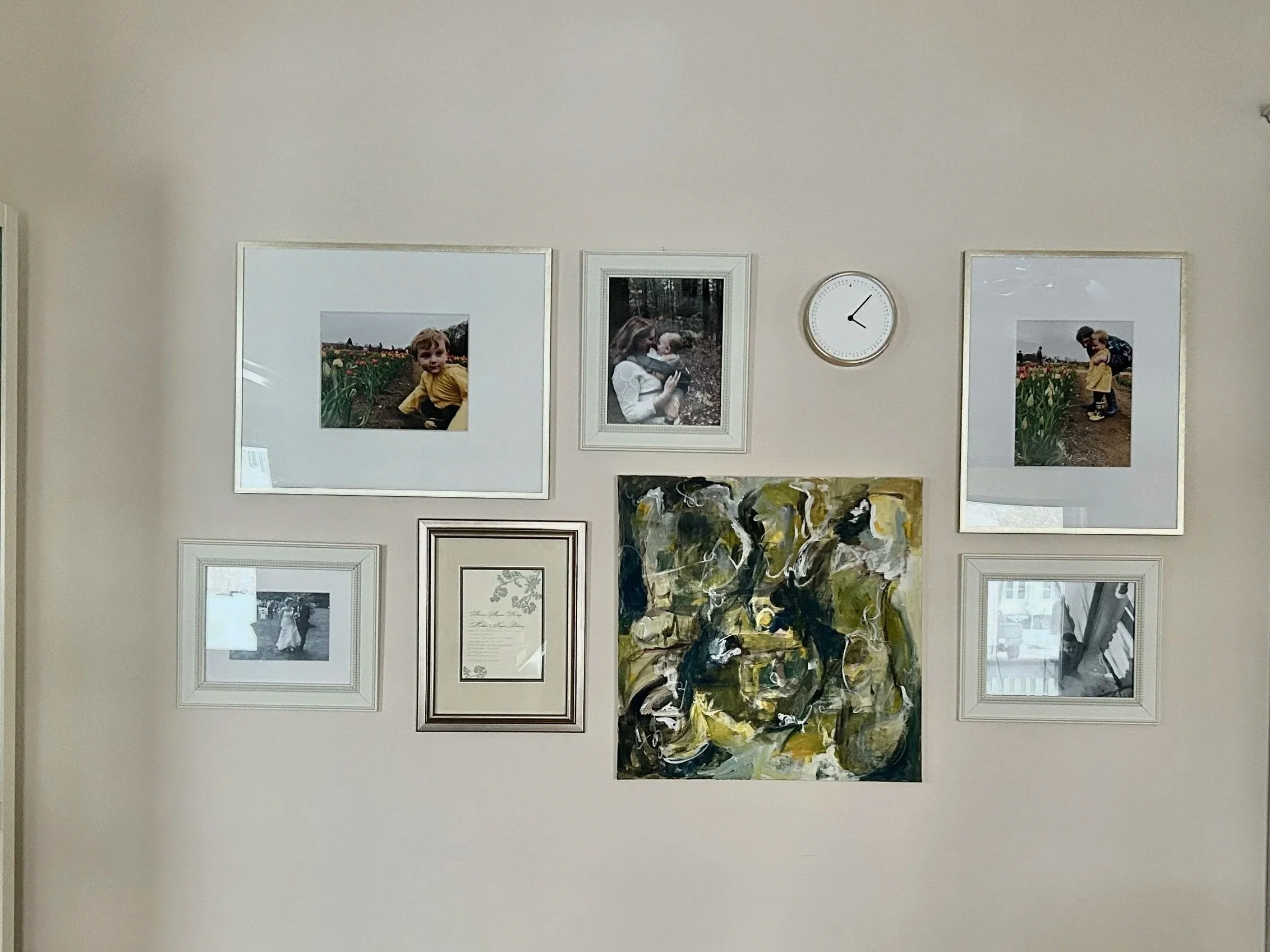 Wall with a gallery of framed photographs, an abstract painting, and a white clock showing 12:05.