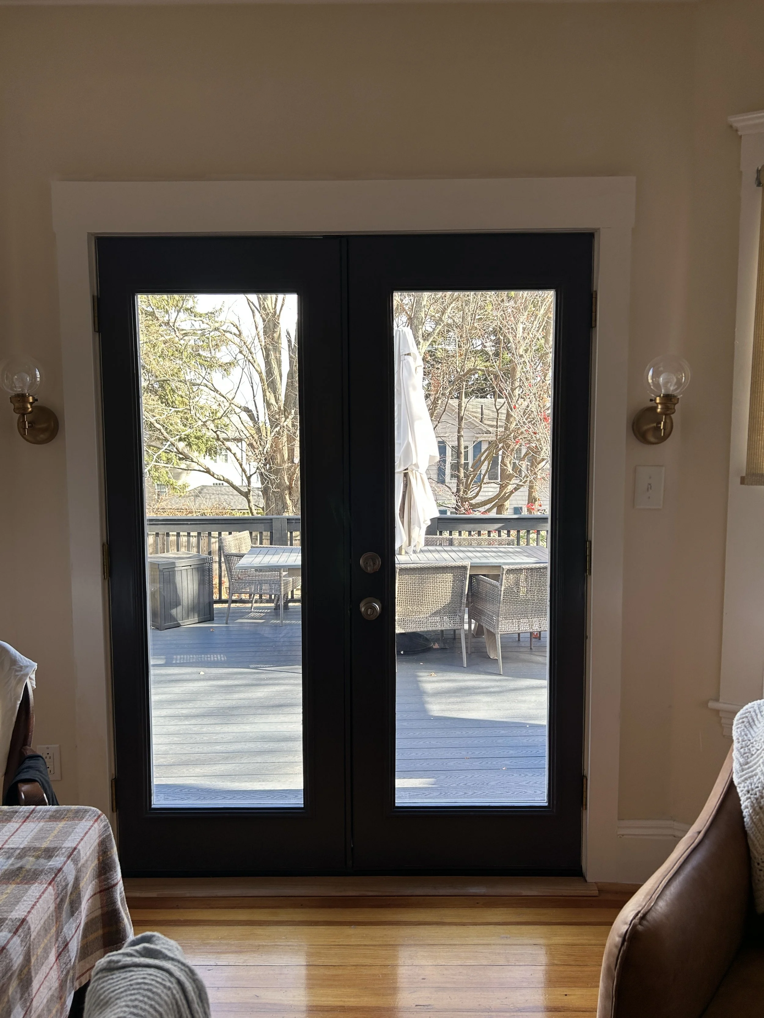Interior view of black double glass doors leading to an outdoor deck with patio furniture and an umbrella.