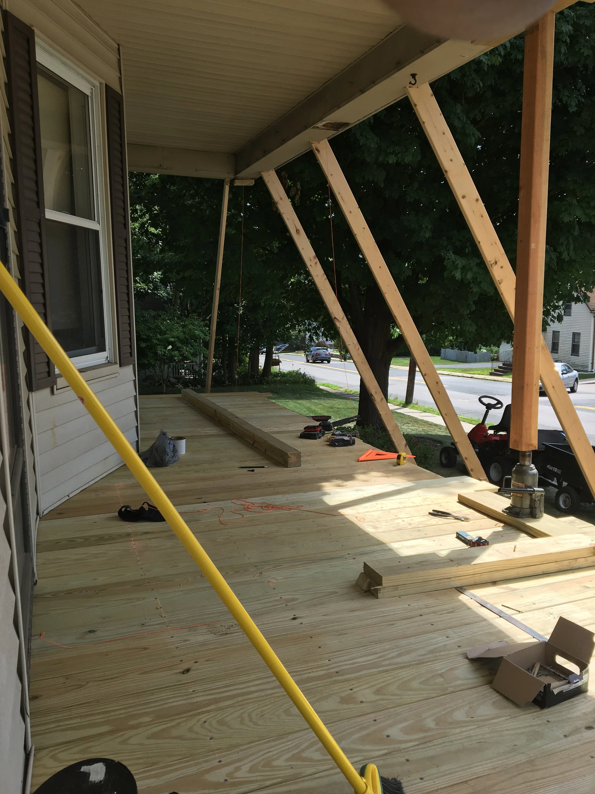A house porch under construction with a new wooden deck, supported by angled wooden beams, and tools scattered around.