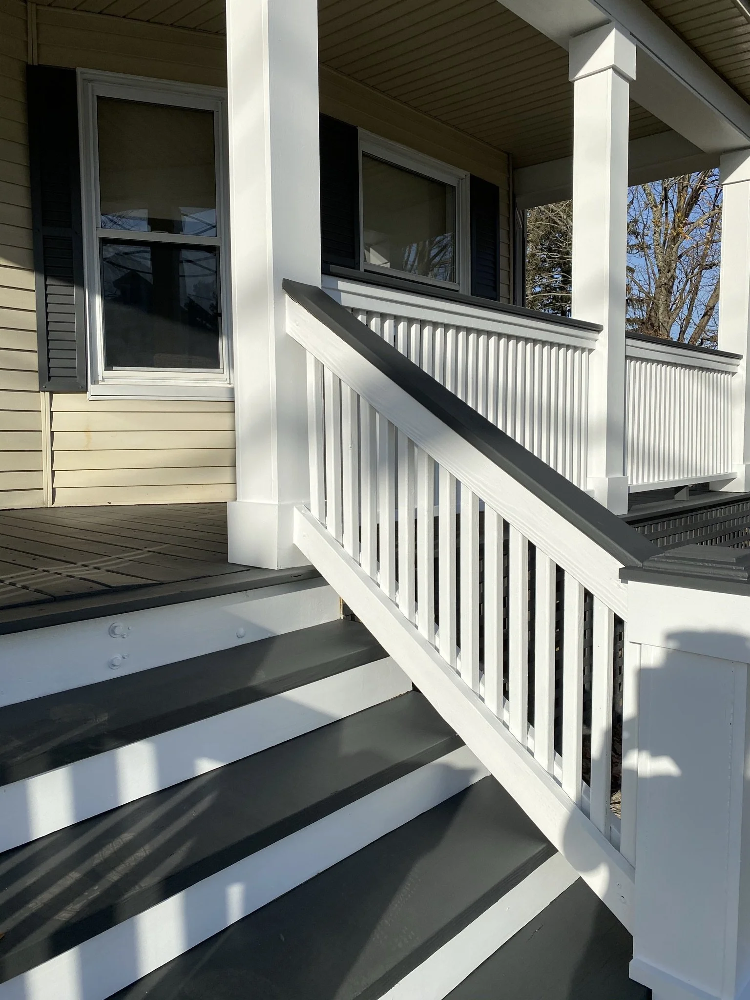 Front porch of a house with stairs, white railing, and a window.