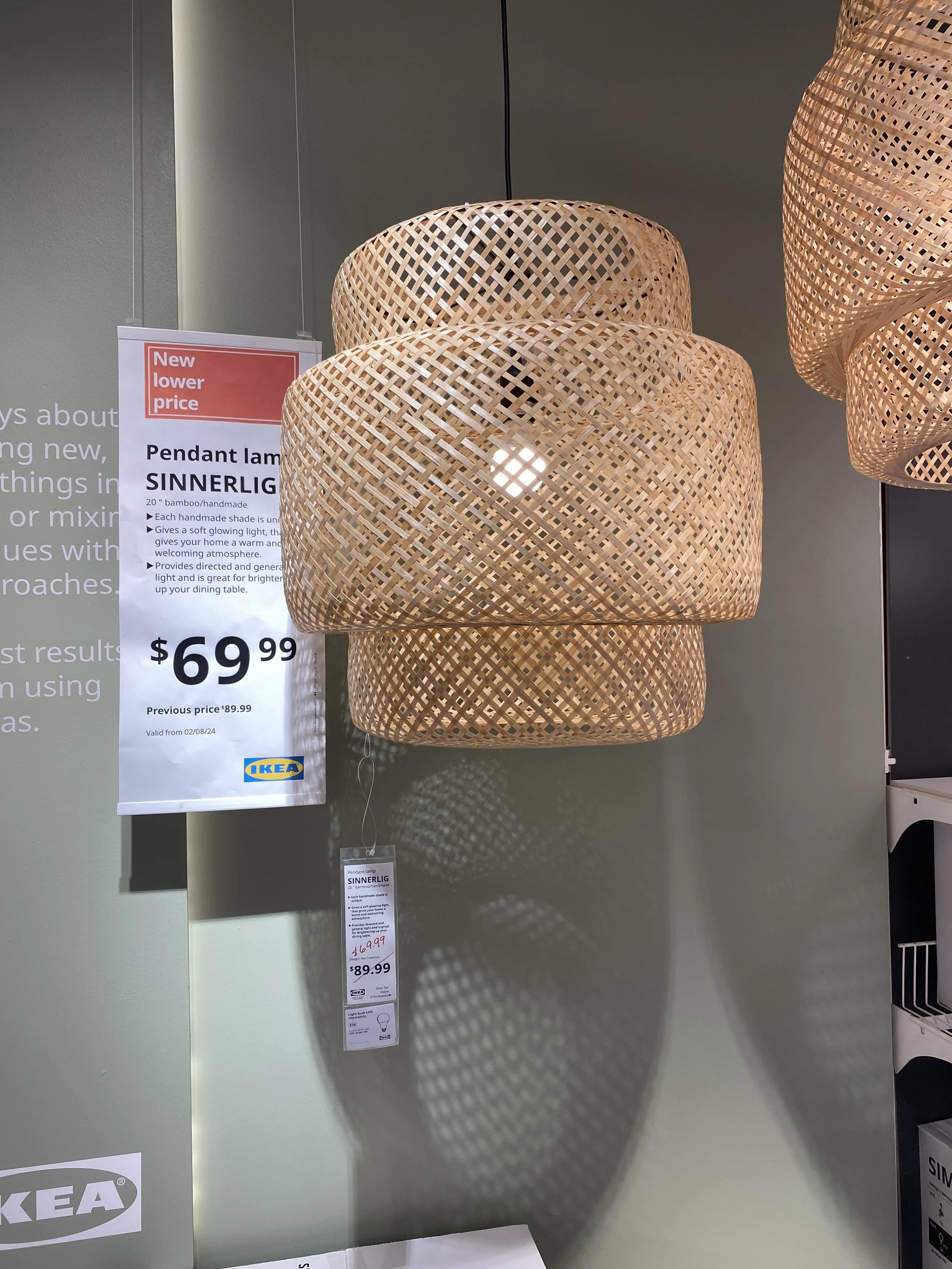 A woven bamboo pendant lamp on display at IKEA, with a price tag of $69.99, hanging beside a sign advertising the lamp with details and previous price.
