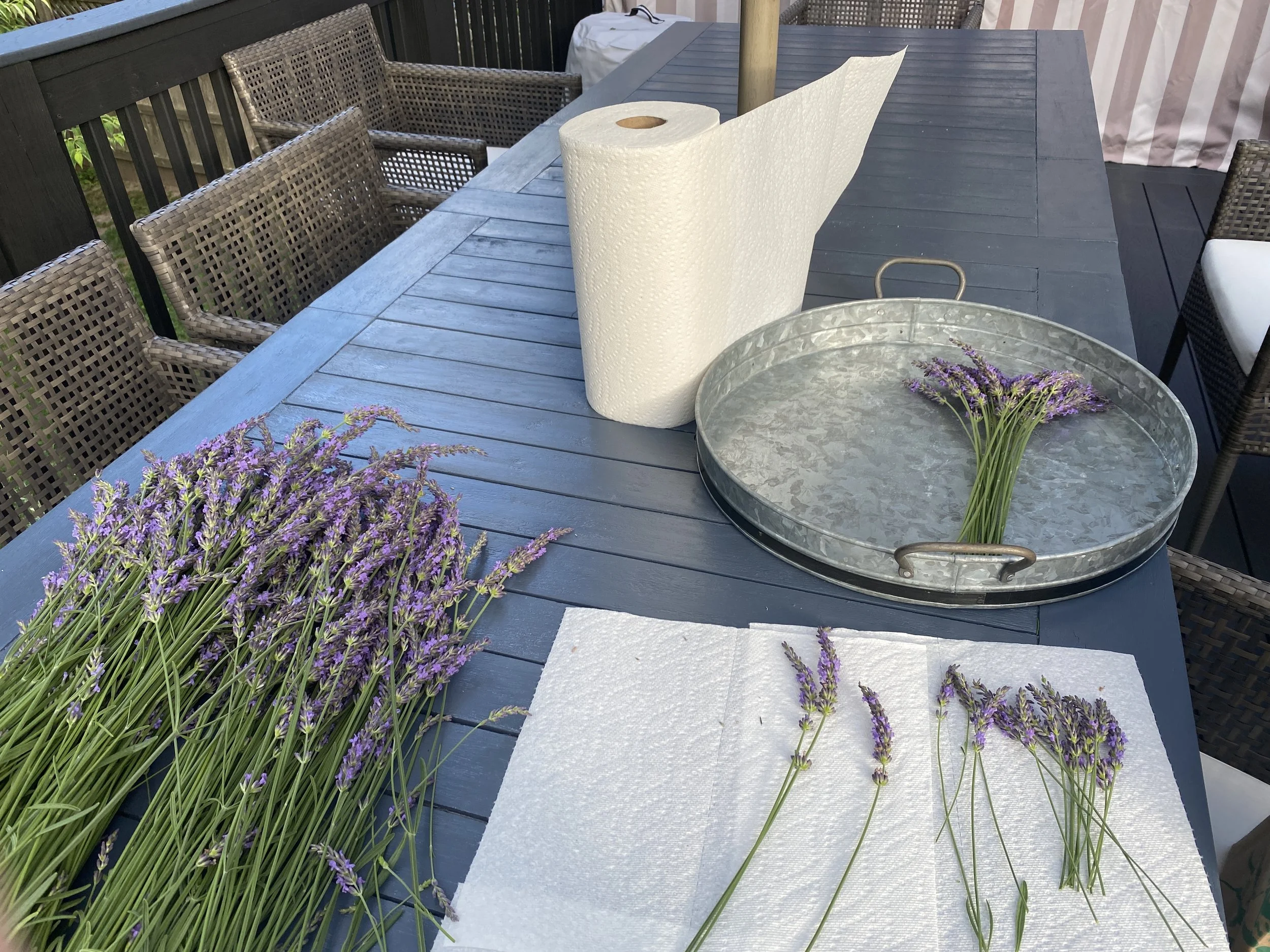 Outdoor table with lavender flowers, paper towels, and a metal tray, with chairs around the table.