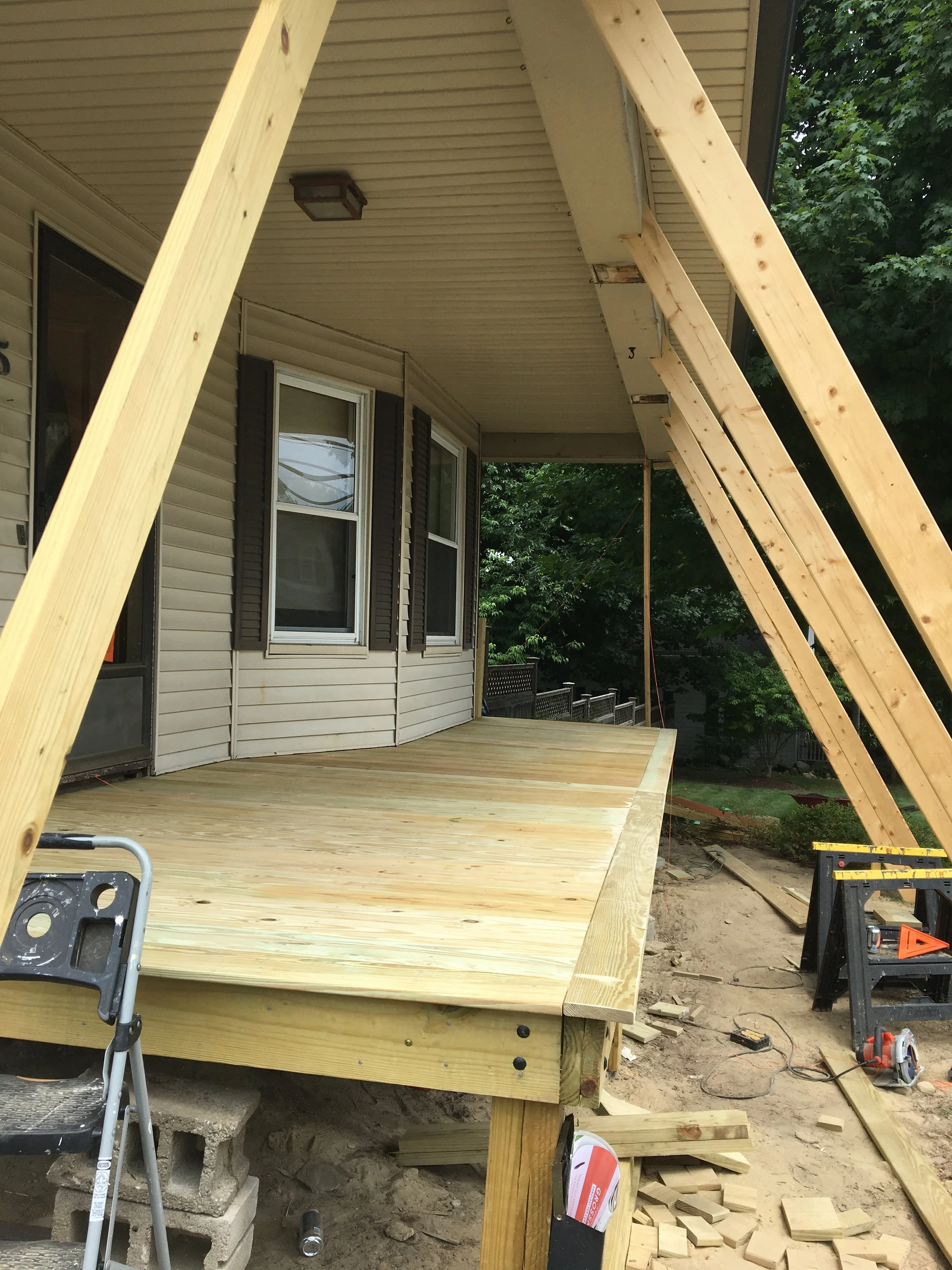 Construction of a new wooden deck attached to a residential house, with unfinished support beams and tools visible.