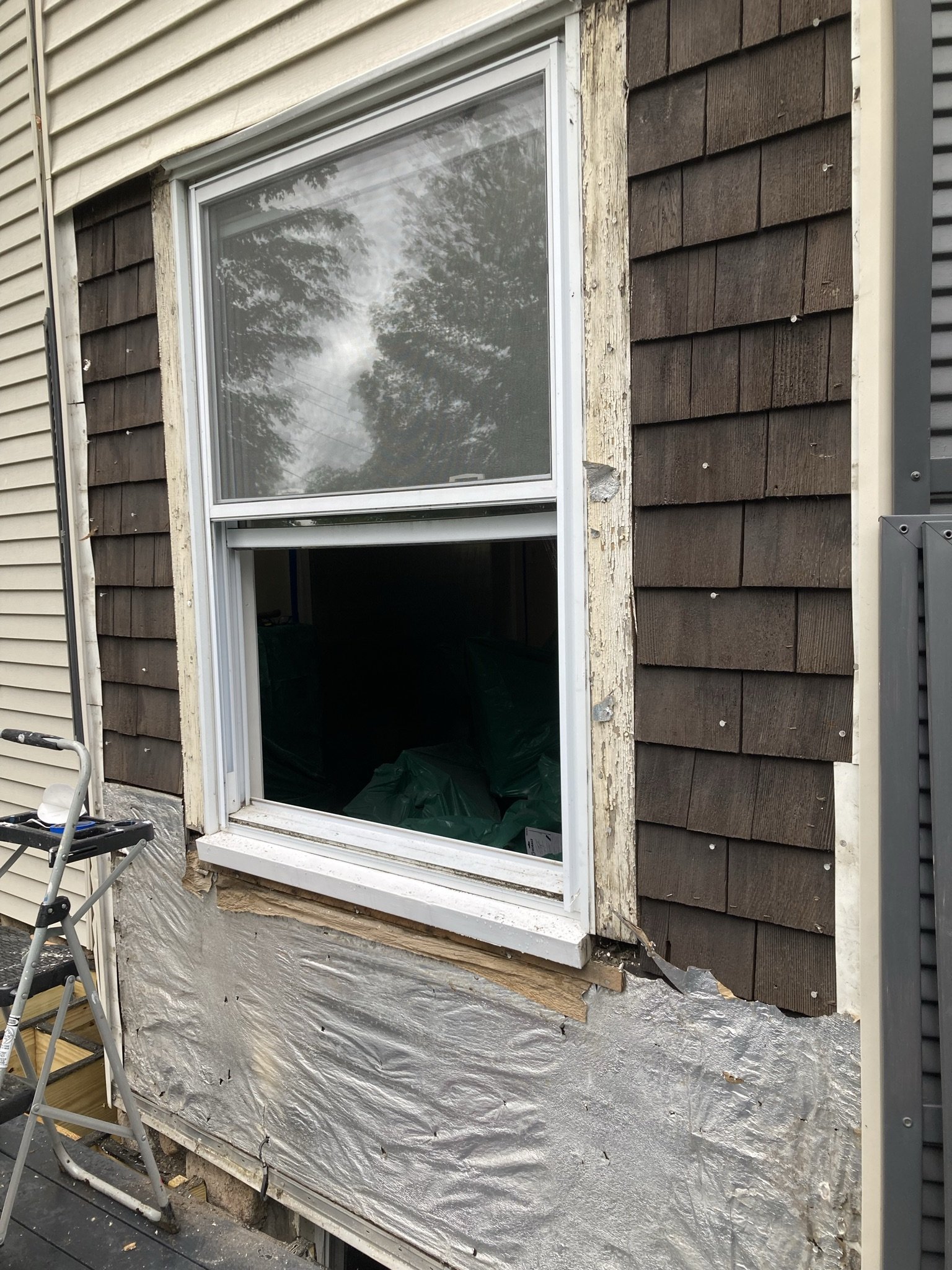 A house window with the exterior wall undergoing renovation, showing old wood siding and insulation material.